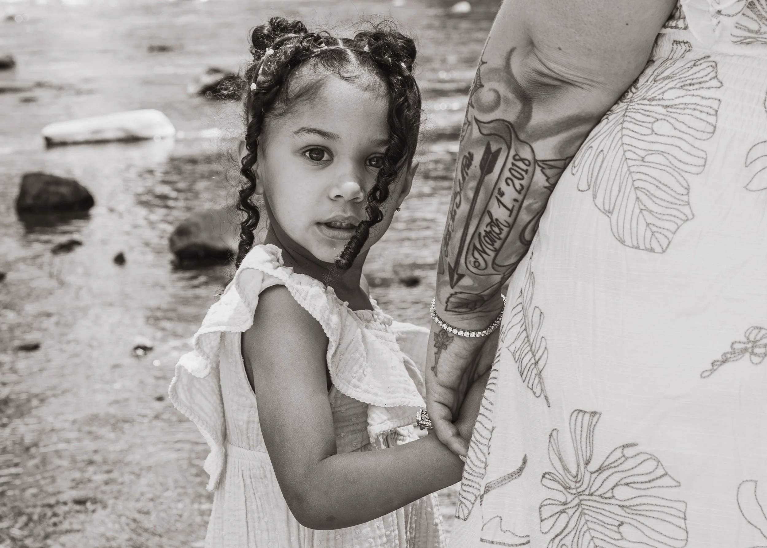 A young girl holding hands with an adult standing by a rocky riverbank.