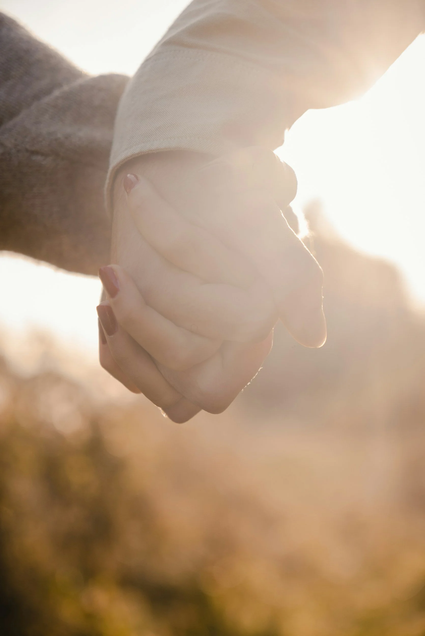Close-up of two hands holding each other with sunlight in the background, outdoors.