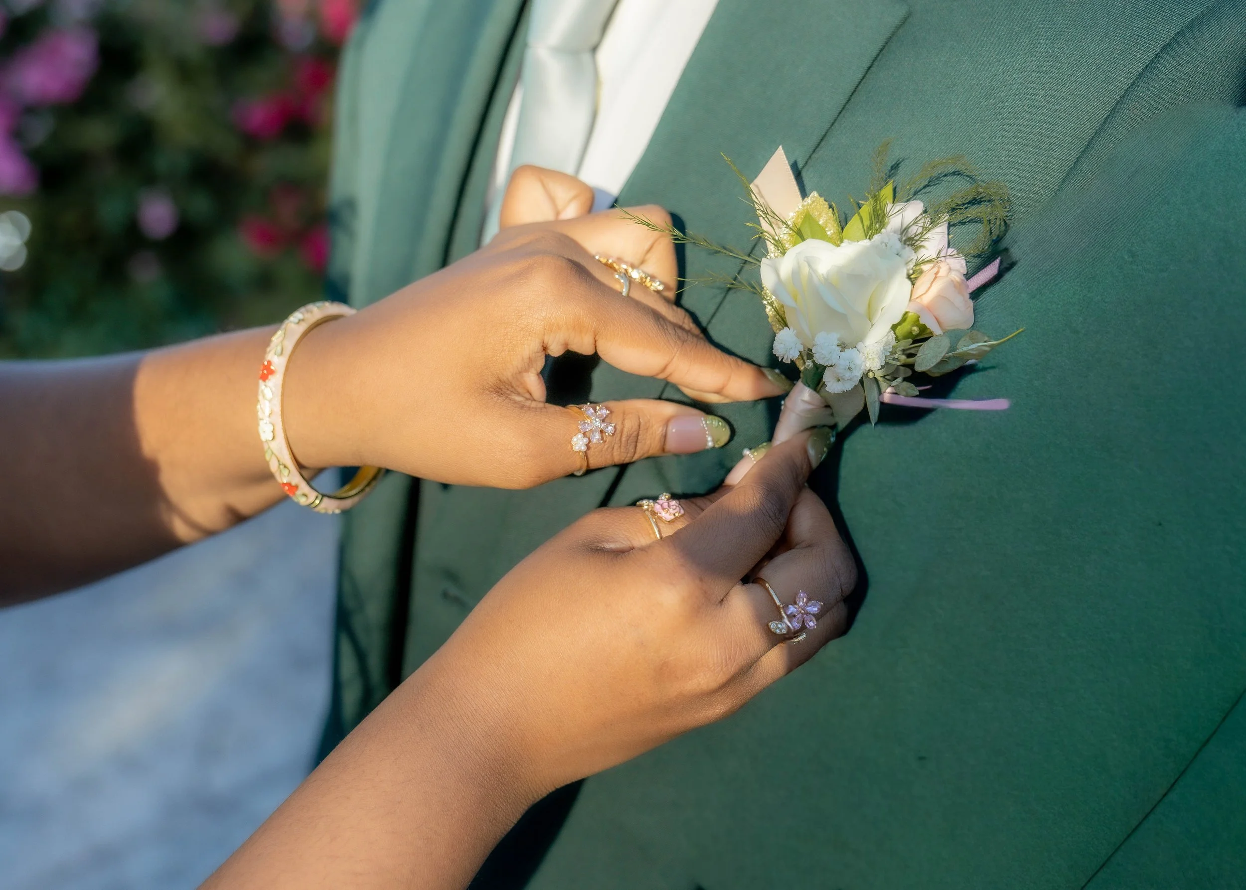 Hands adjusting a white boutonniere on a green suit jacket.