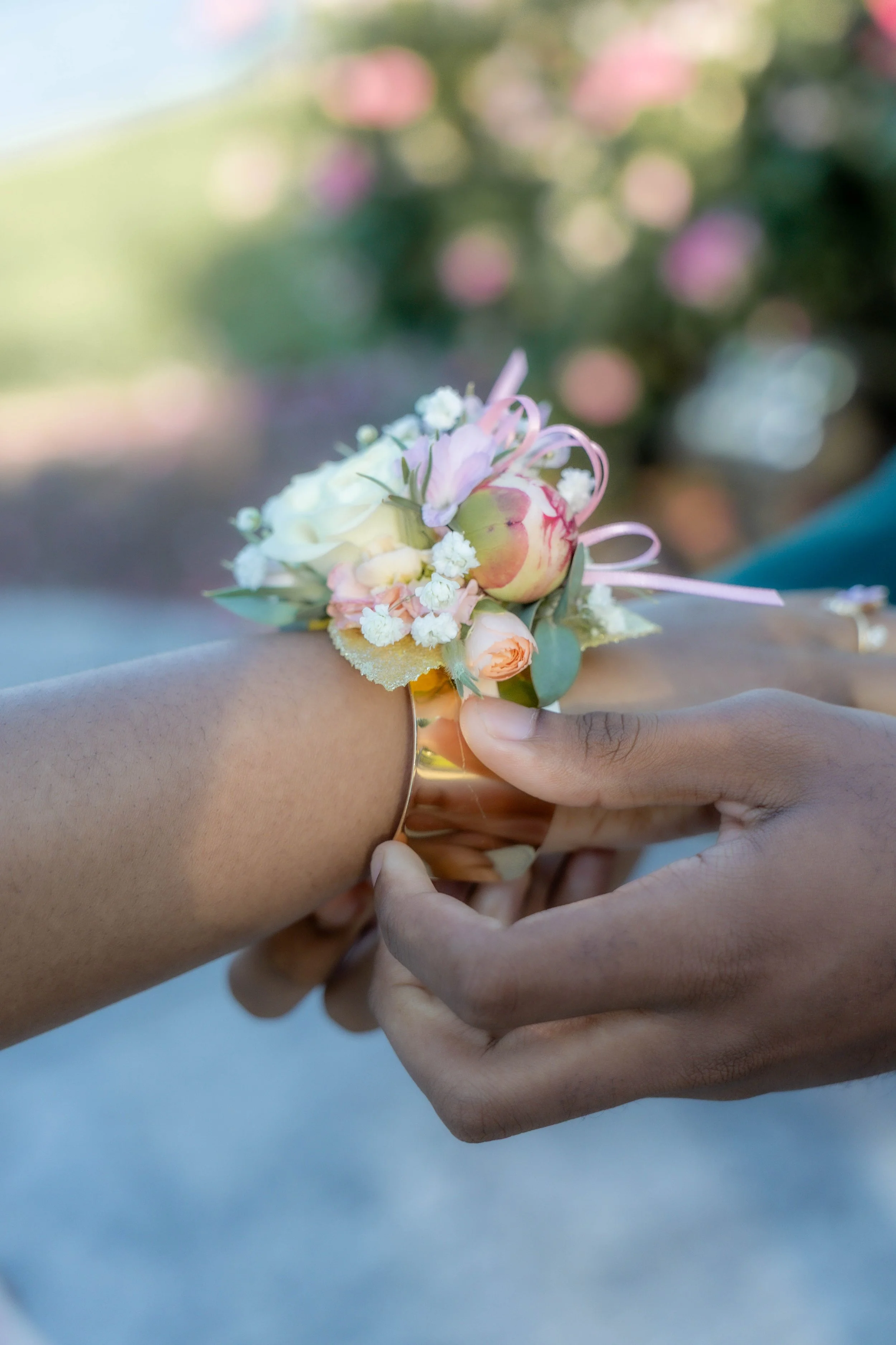 Close-up of hands pinning a boutonniere with pink, white, and peach flowers on someone's arm for a formal event.