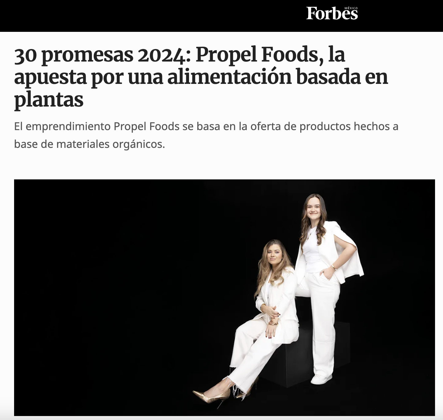 Dos mujeres con vestimenta blanca, una sentada y otra de pie, posando en un fondo negro en una fotografía de estilo profesional.