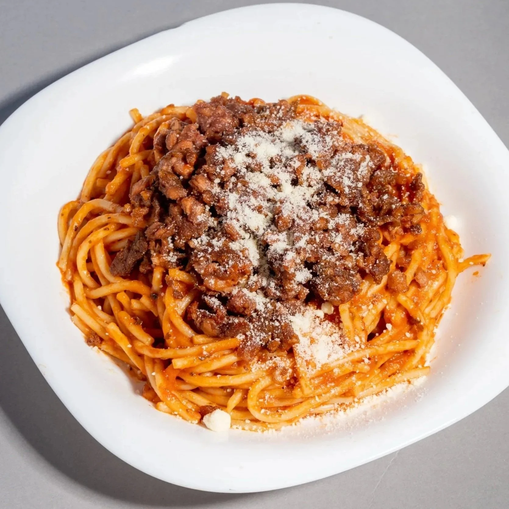 Plato de espaguetis con salsa de carne plant based y queso rallado en un plato blanco.