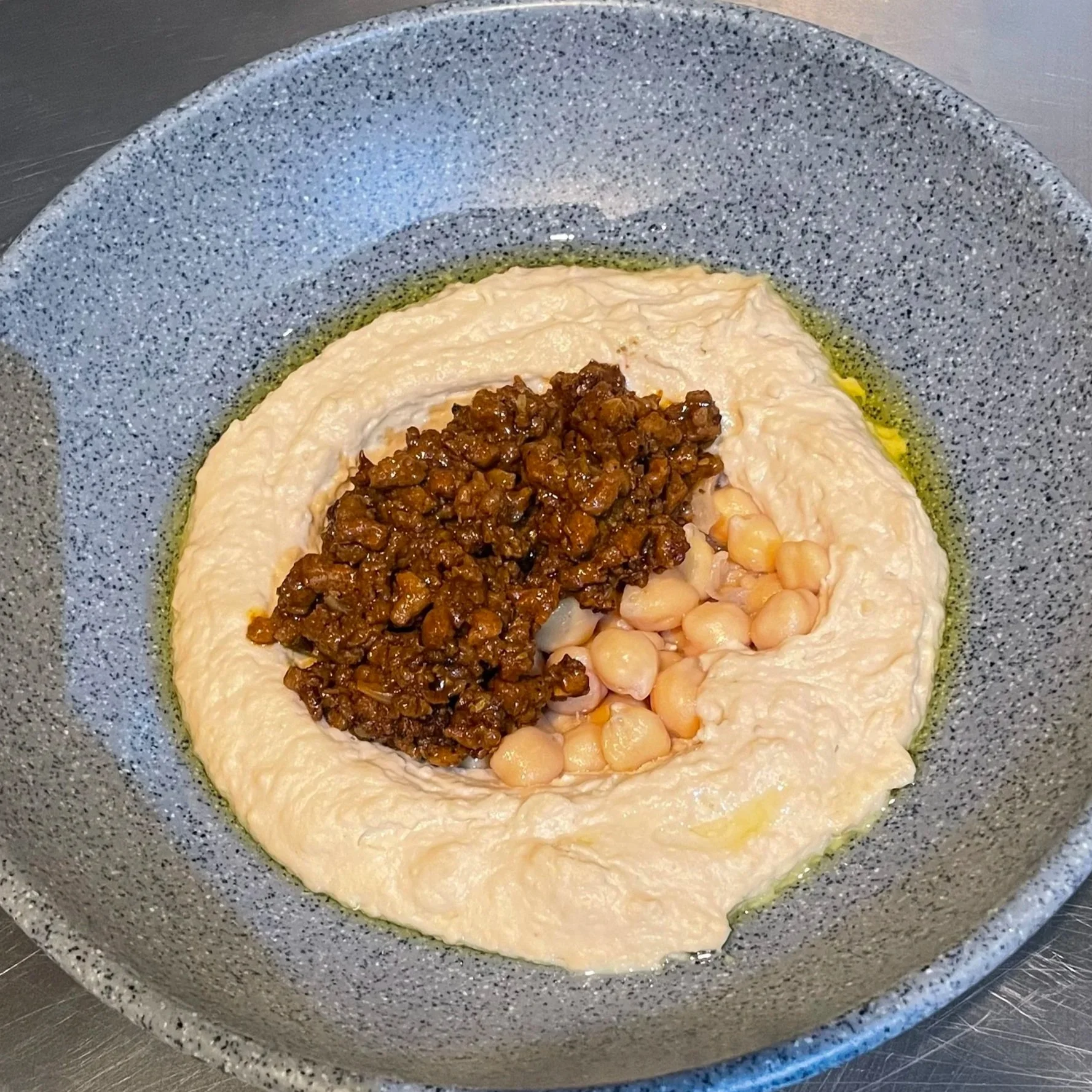 Plato de puré de garbanzos decorado con carne molida vegana y garbanzos cocidos, en un plato de cerámica gris.