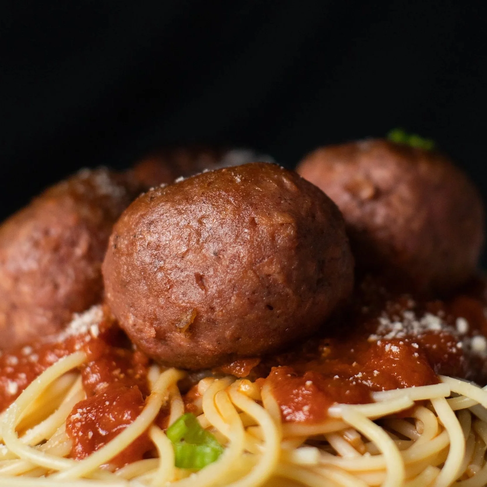 Albóndigas de carne plant based con spaghetti y salsa de tomate, decoradas con queso parmesano y cebolla picada.