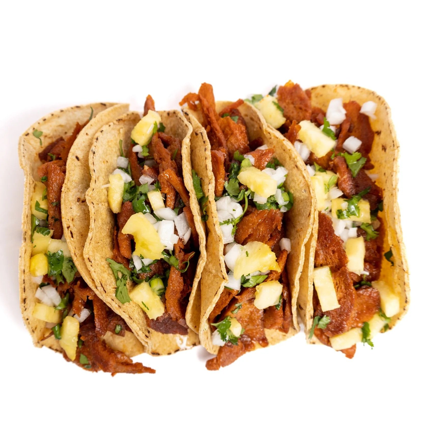Tres tacos de pastor vegano con cebolla, cilantro y piña, en tortillas de maíz.