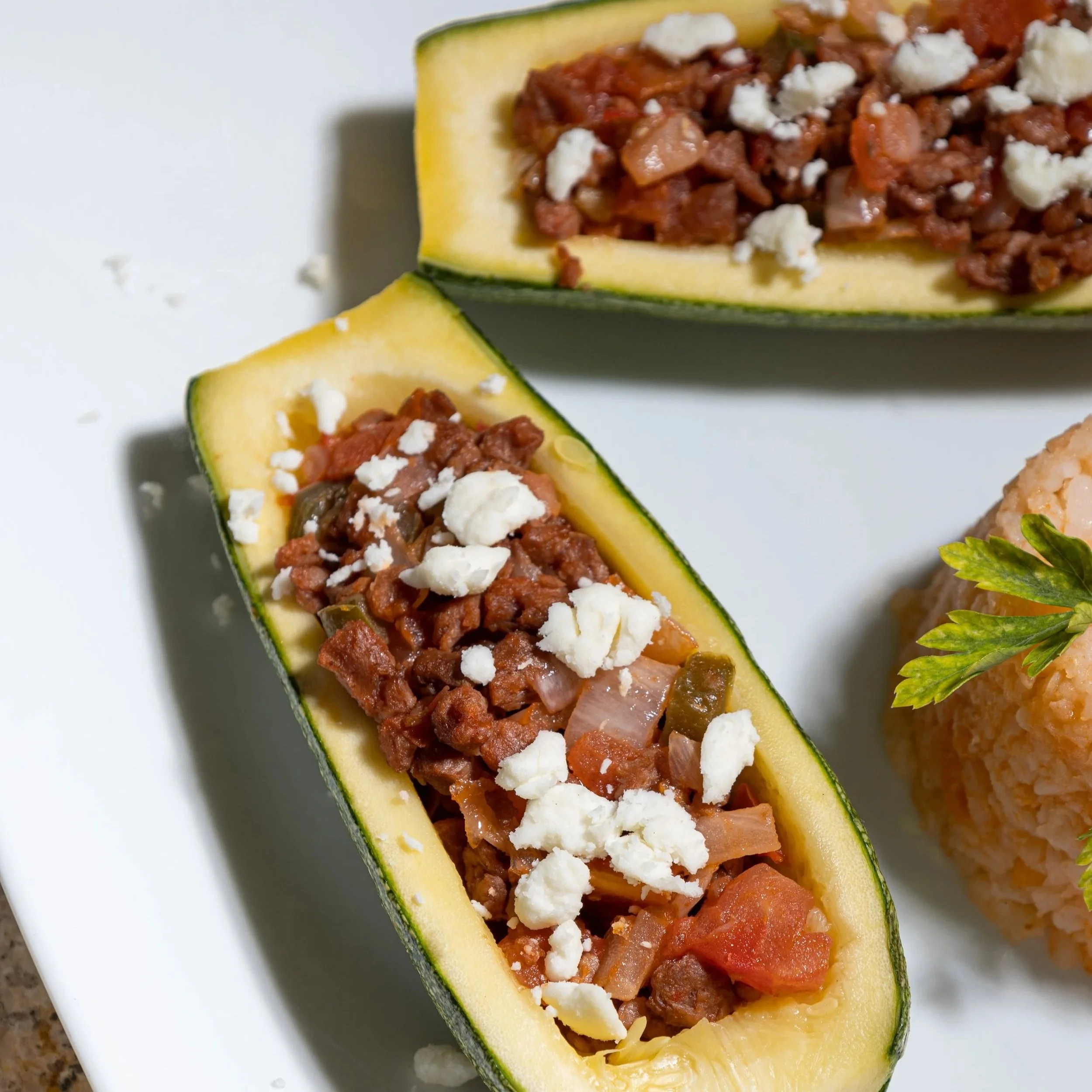 Calabaza rellena con carne vegana, cebolla, tomate, y queso desmenuzado en un plato blanco.