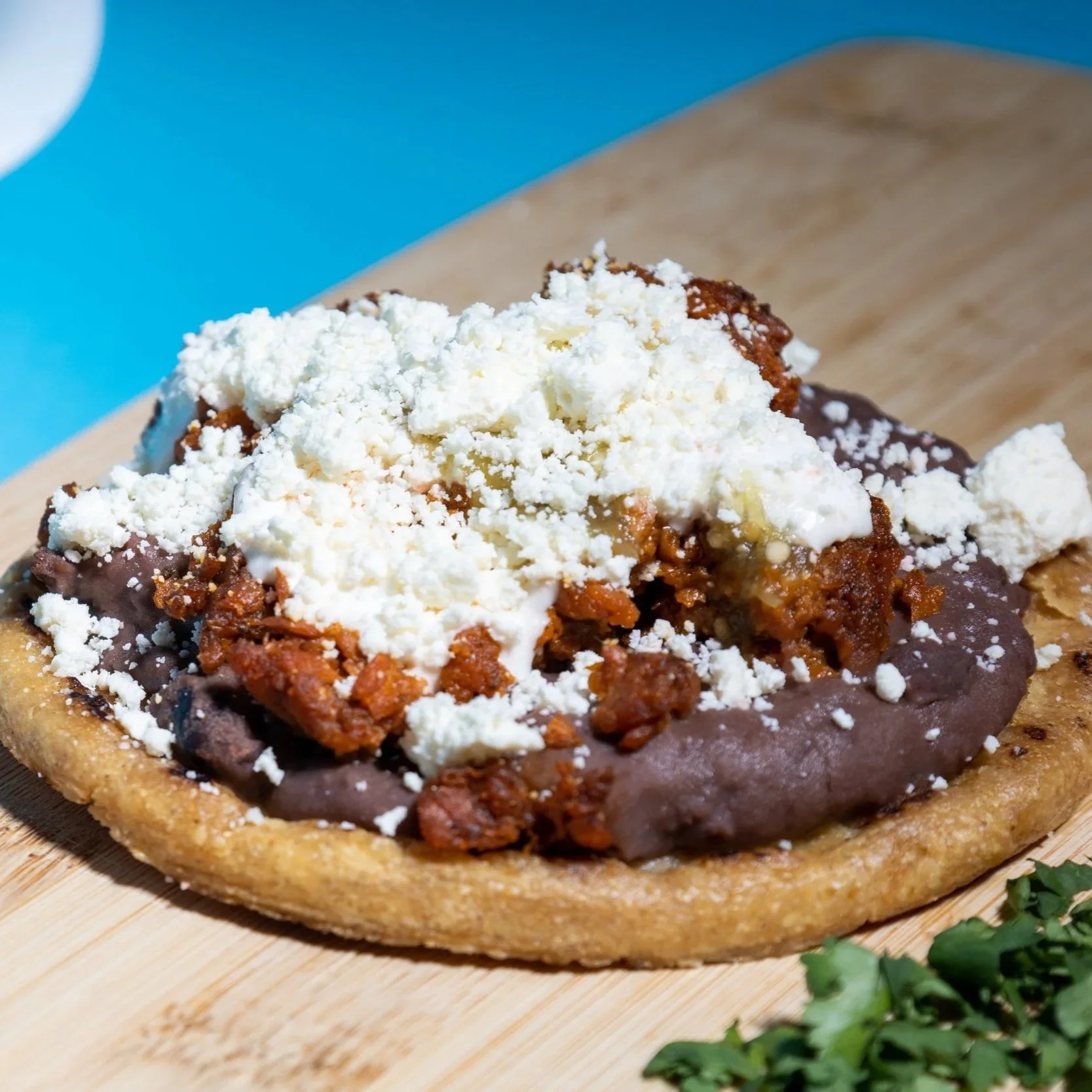 Sope con frijoles refritos, chorizo plant based, queso rallado y crema