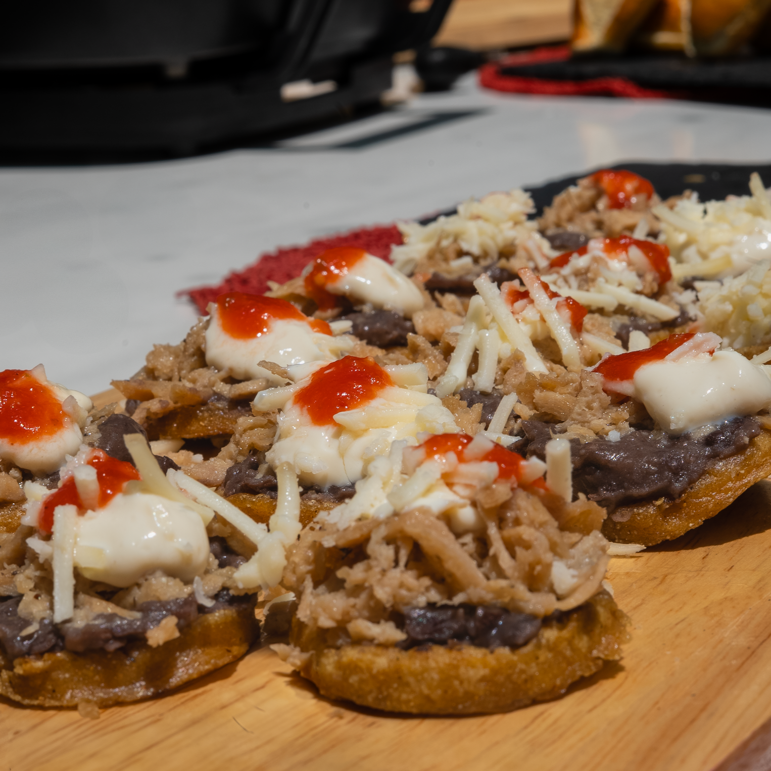 Sopes de pollo deshebrado vegano con queso rallado, crema y salsa en un plato de madera