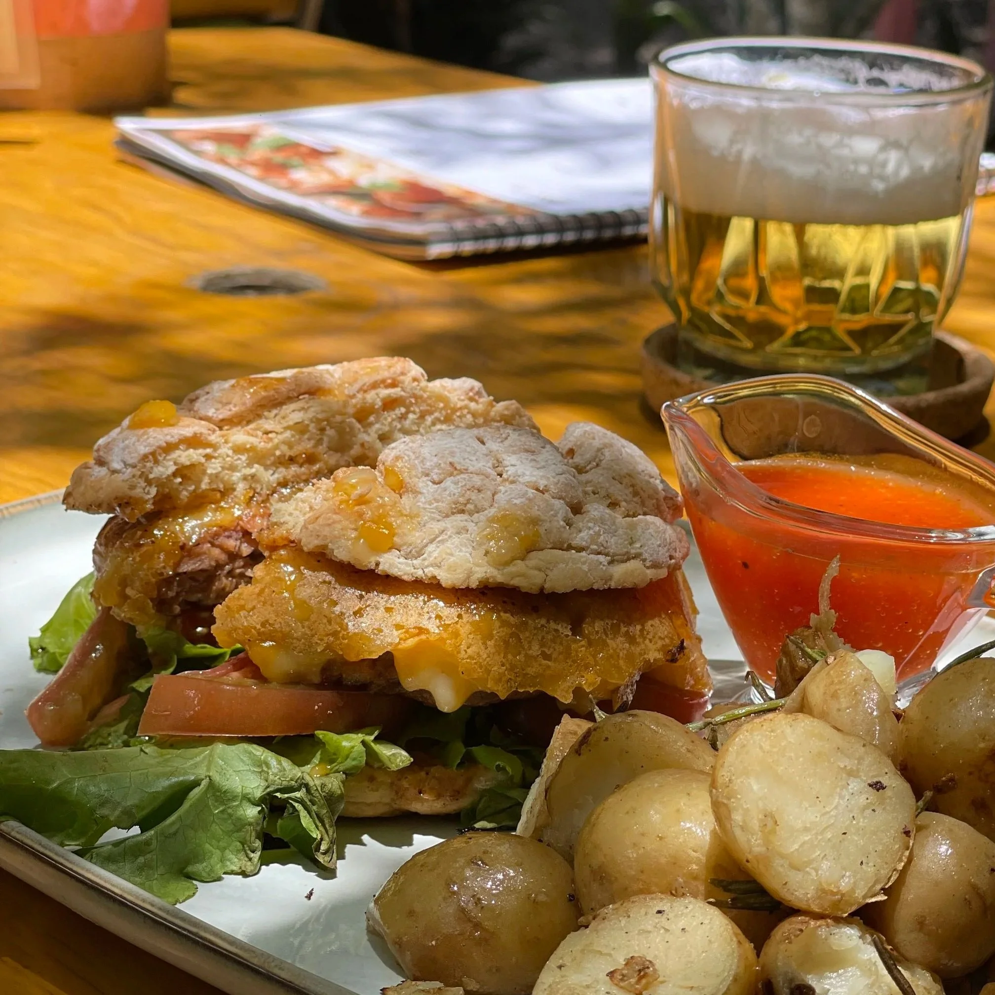 Imagen de una comida con una hamburguesa con papas, salsa, y una bebida en una mesa de madera.