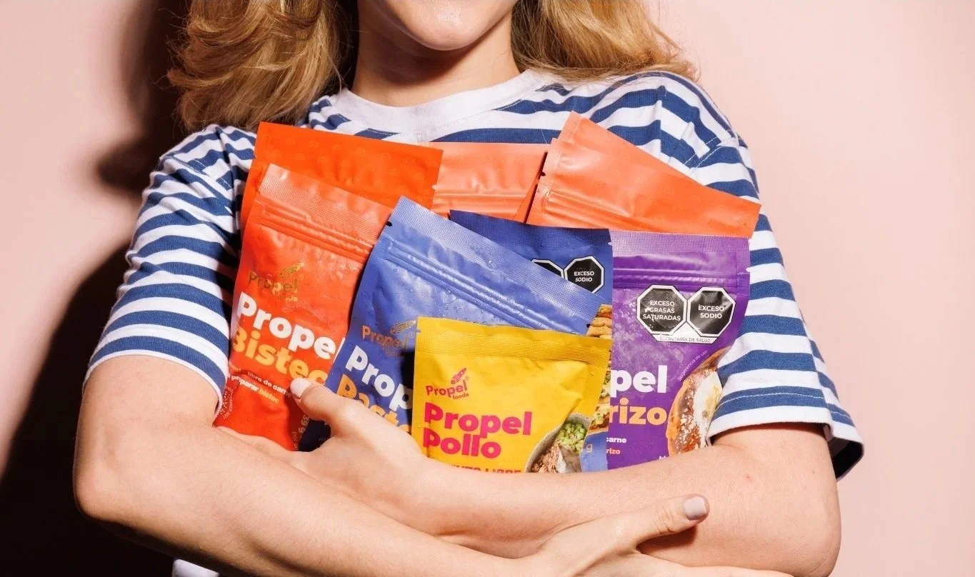 Una persona sostiene varias bolsas de condimentos de sabores diferentes, incluyendo pollo, bistec, y arroz.