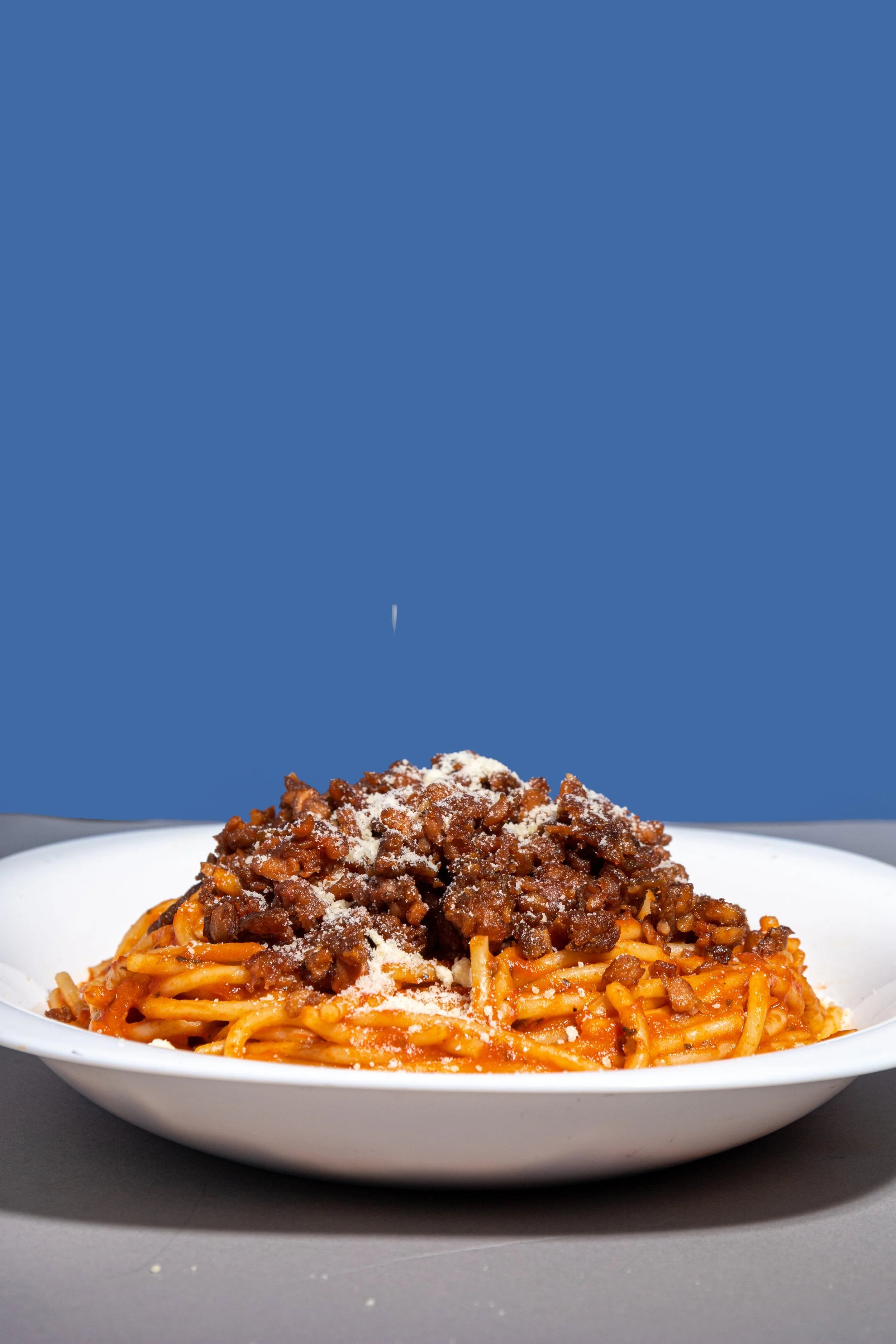 Plato de espaguetis con molida plant based y salsa de tomate, espolvoreado con queso rallado, en un plato blanco.