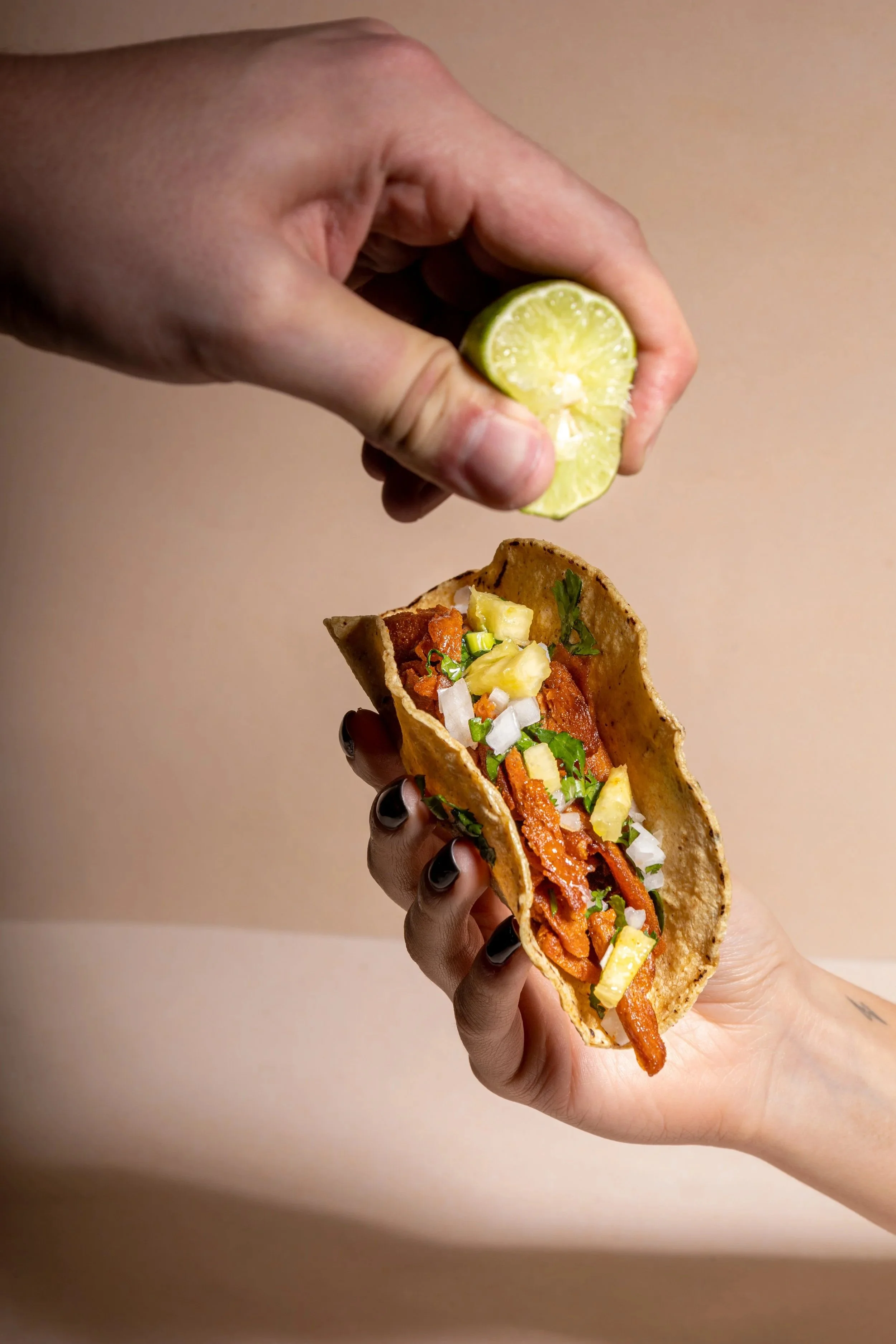 Persona exprimiendo jugo de lima sobre un taco con pastor plant based, cebolla, cilantro y piña.