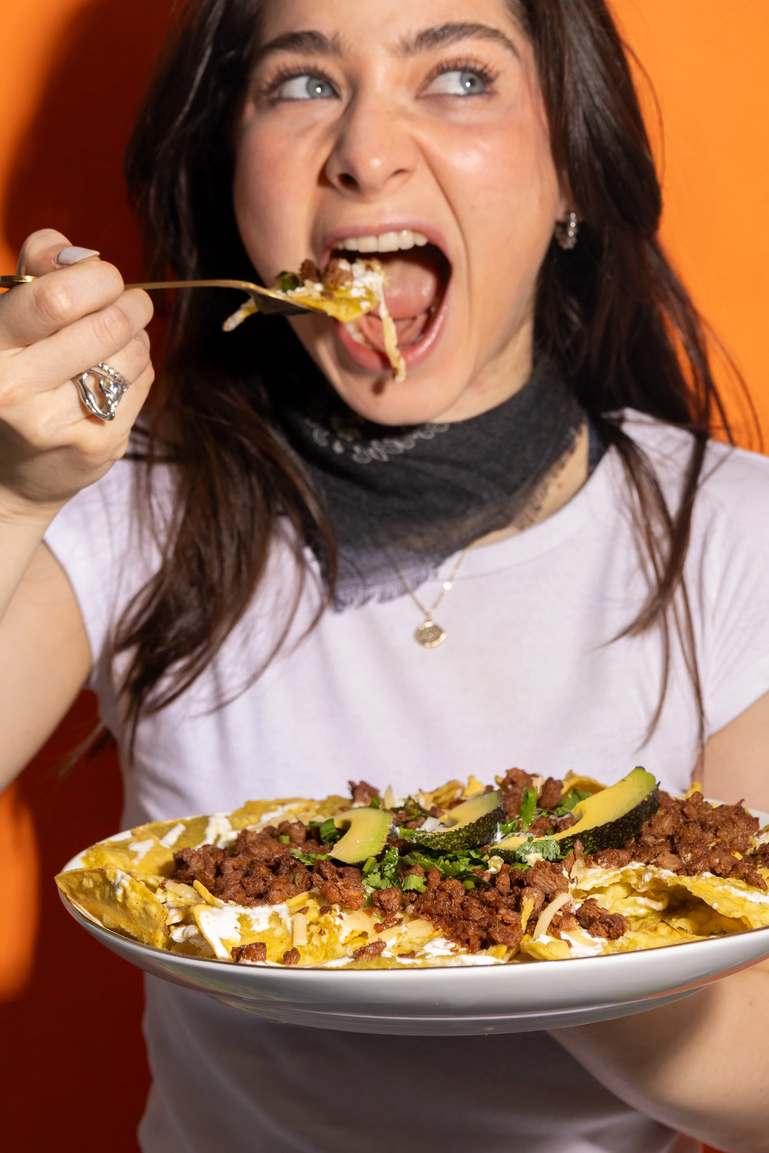 Mujer comiendo un plato grande de nachos con carne, frijoles, aguacate, queso y otros ingredientes.