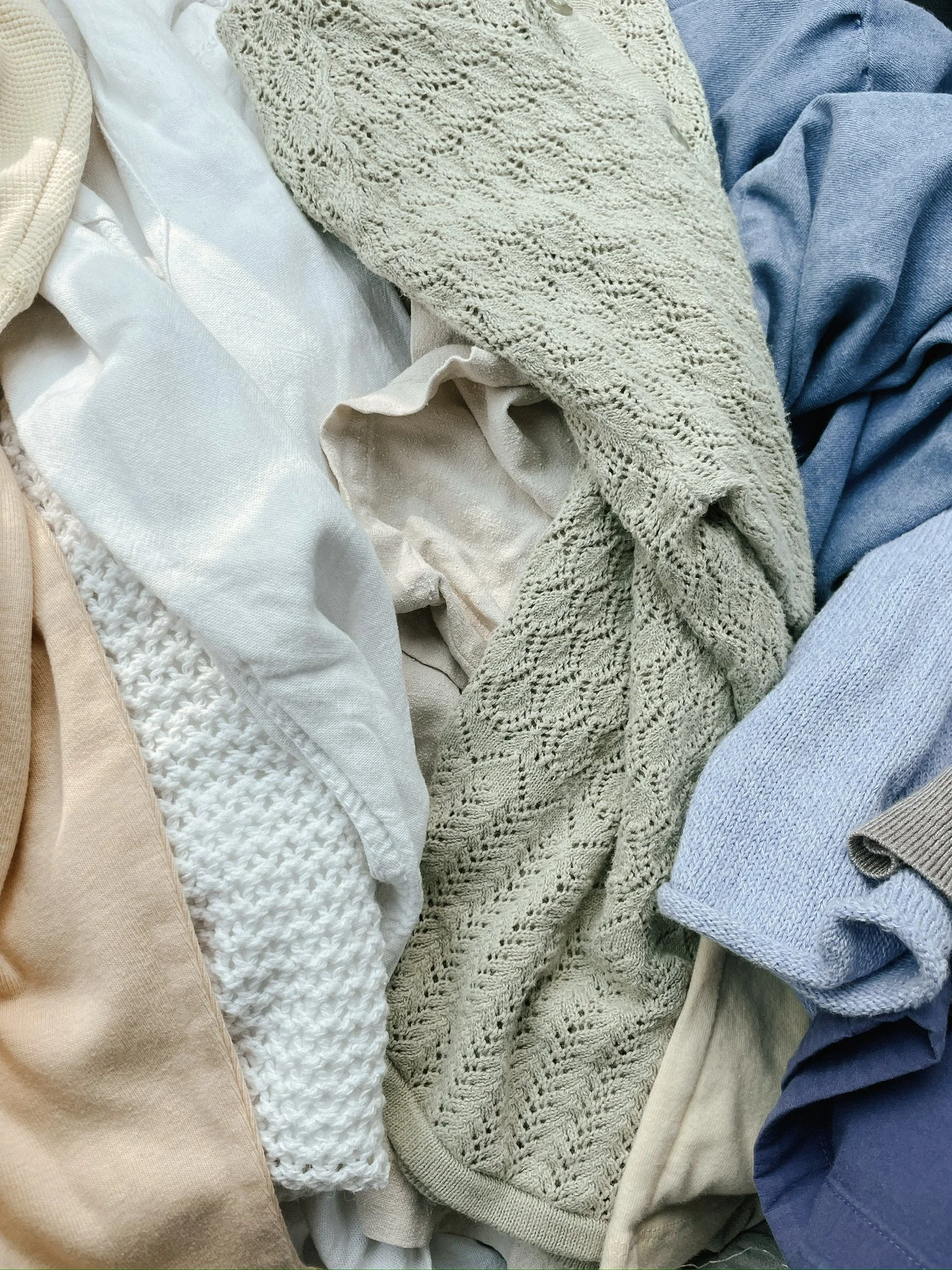 A pile of assorted clothes in various colors and textures, including white, beige, green, blue, and gray fabrics.