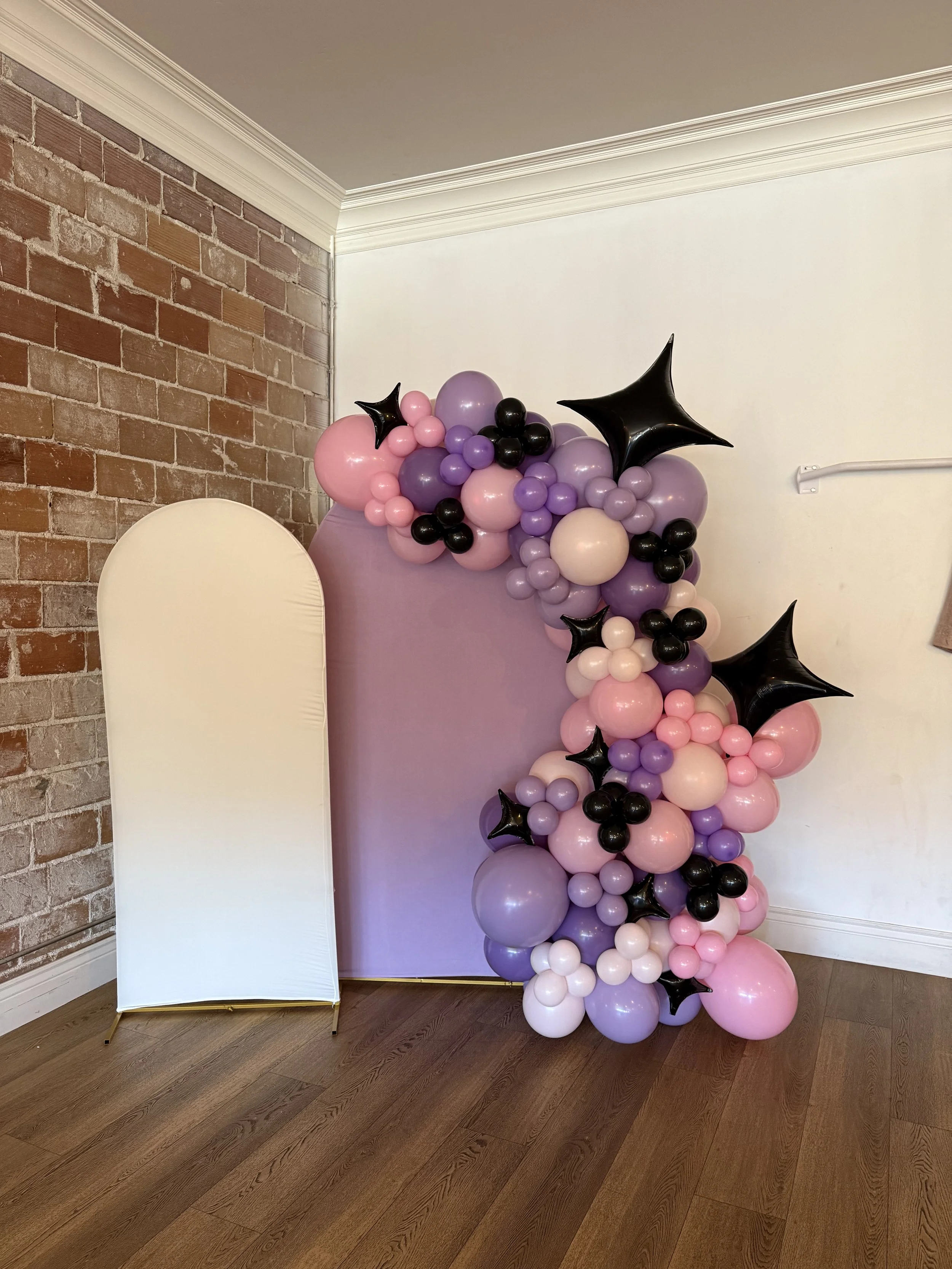 Decorative balloon display with pink, purple, black, and white balloons arranged against a backdrop.