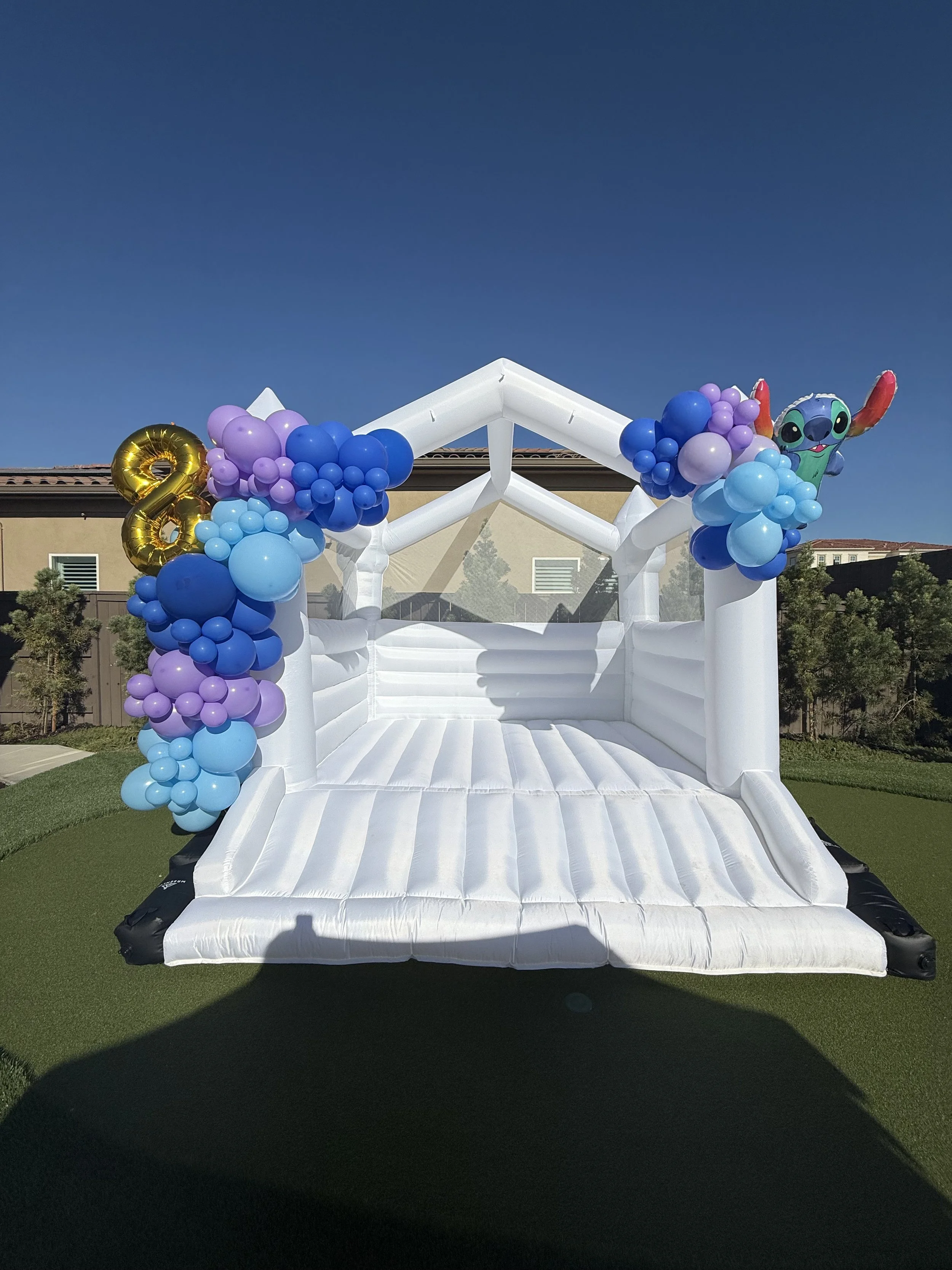 Inflatable bounce house decorated with purple, blue, and light blue balloons, with a gold number 8 balloon and a Stitch character balloon at the top corner.