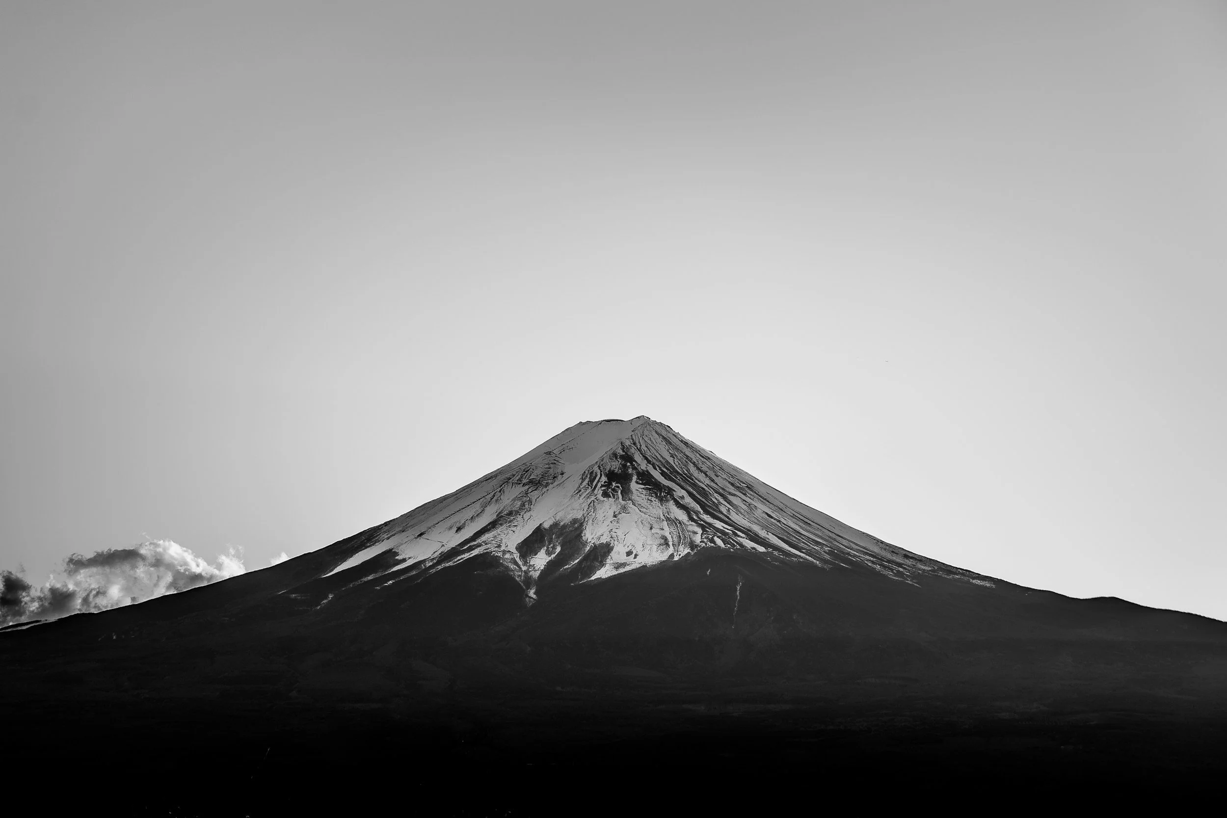 A black and white photo of Mount Fuji with snow on its peak, under a clear sky.