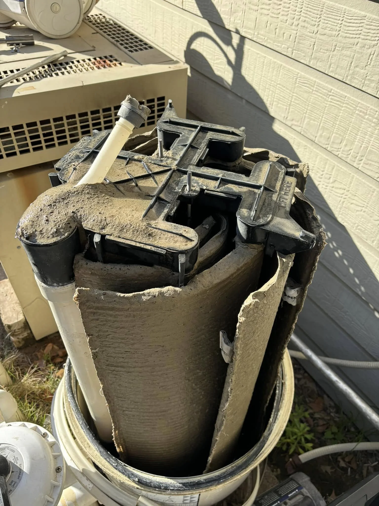 An outdoor air conditioning unit with its cover removed, showing the internal filter and components covered in dust and debris.