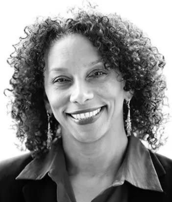 Judge Patricia McGuire. Black and white portrait of a smiling woman with curly hair, wearing earrings and a collared shirt.
