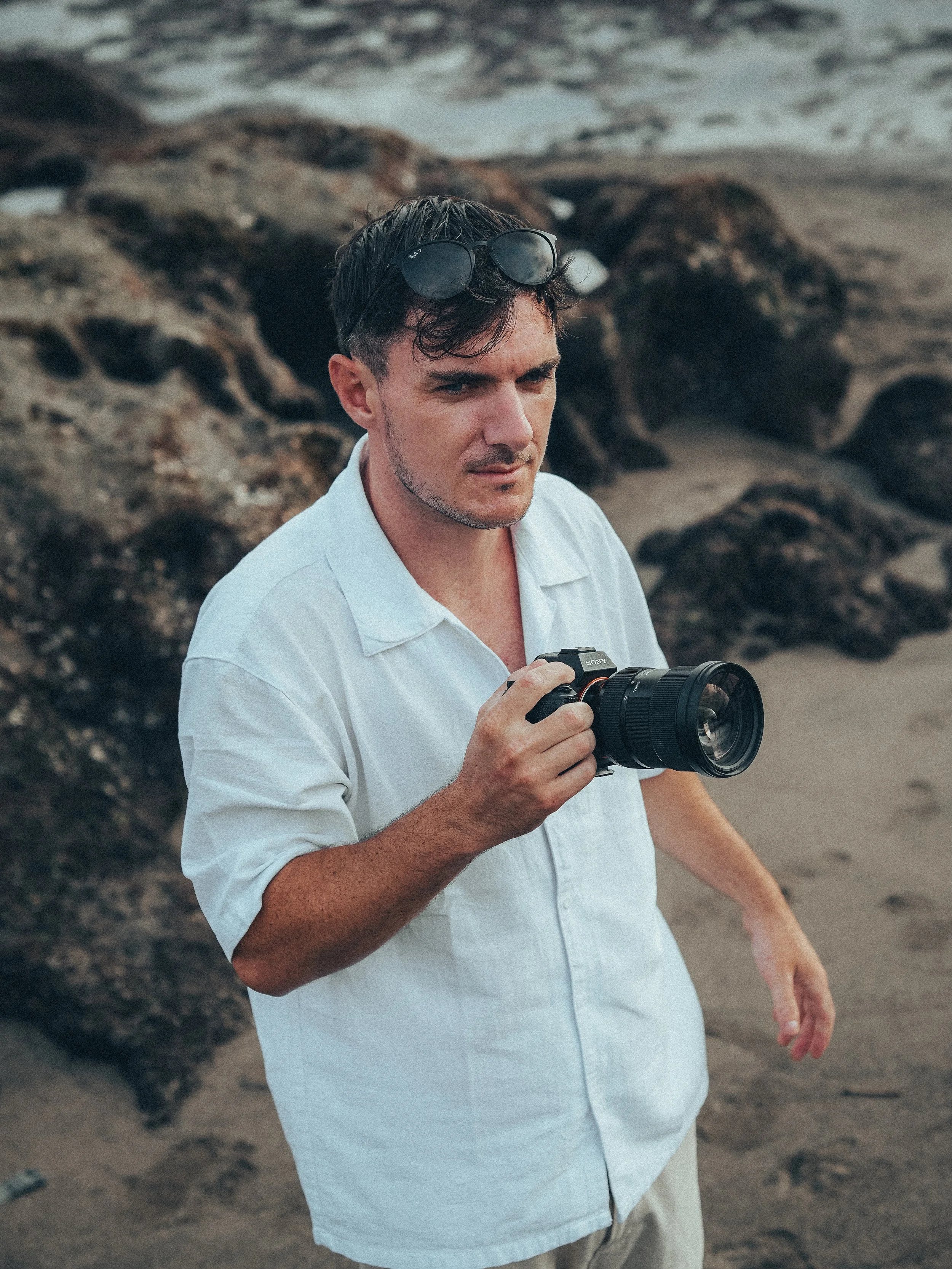 Homme à la plage tenant un appareil photo avec des lunettes de soleil sur sa tête