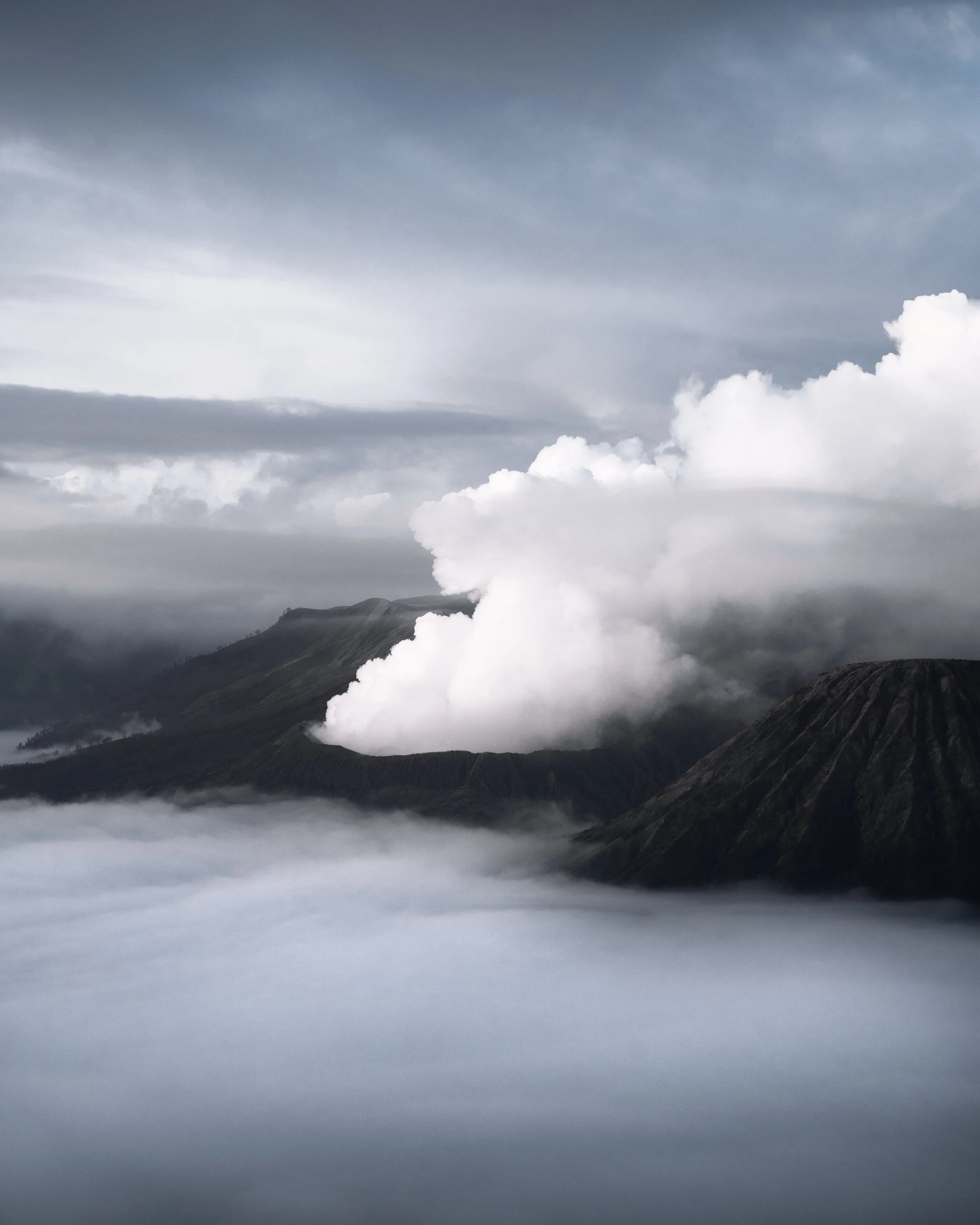 Nuages gris sur un paysage de montagnes avec de la vapeur ou de la fumée blanche s'échappant d'un volcan