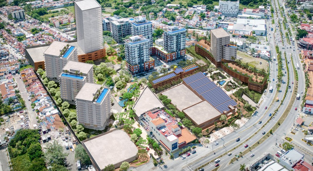 Vista aérea de un complejo urbano con edificios residenciales y comerciales, áreas verdes, y una autopista cercana.