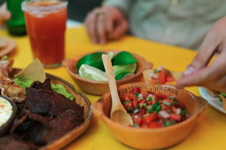 Plato de comida mexicana con carne de res, verduras, y un vaso de salsa roja