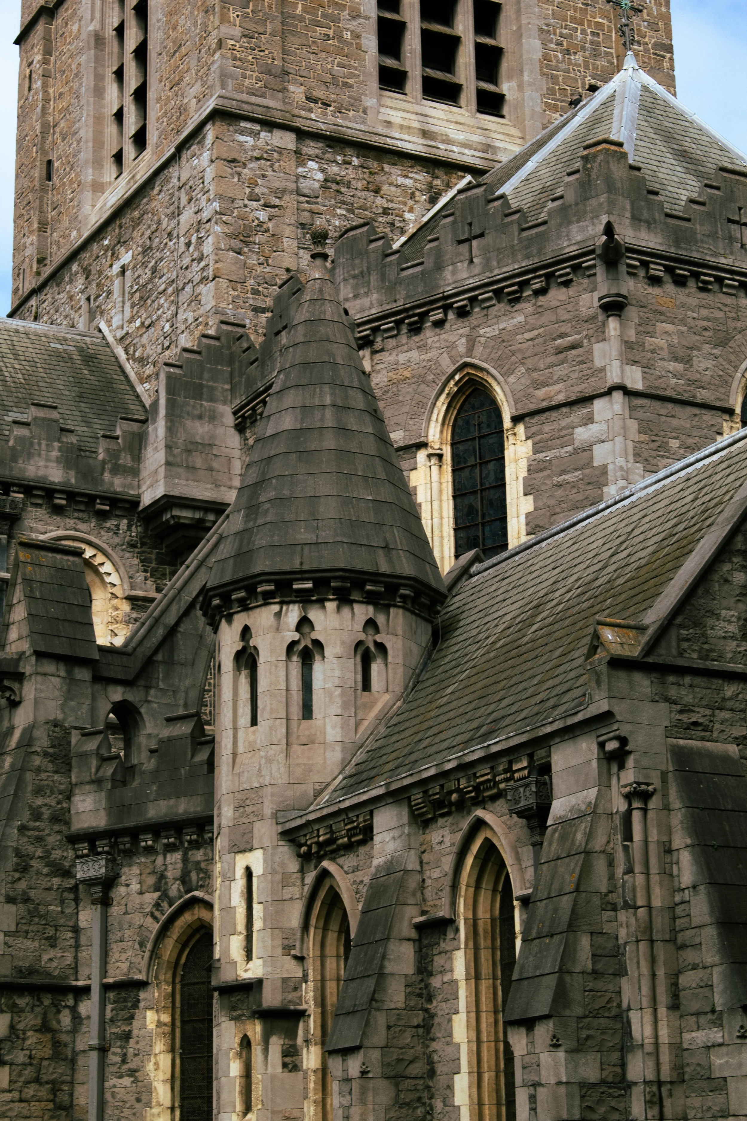 Close-up of an old stone church with gothic-style windows and multiple rooflines, featuring conical turrets and detailed masonry.