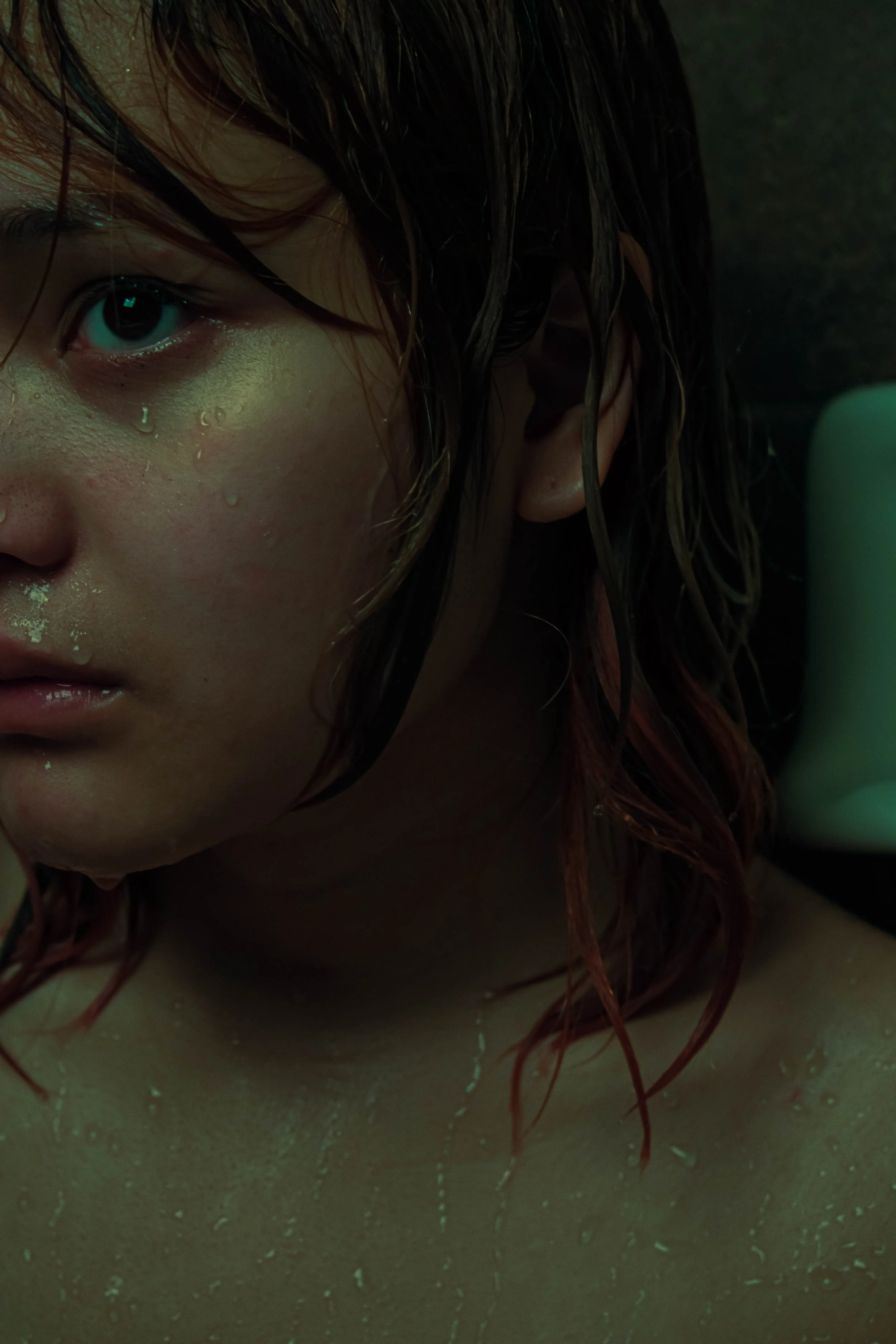 Close-up of a person's wet face with water droplets, with short red hair and dark eyes, partially visible in the image.