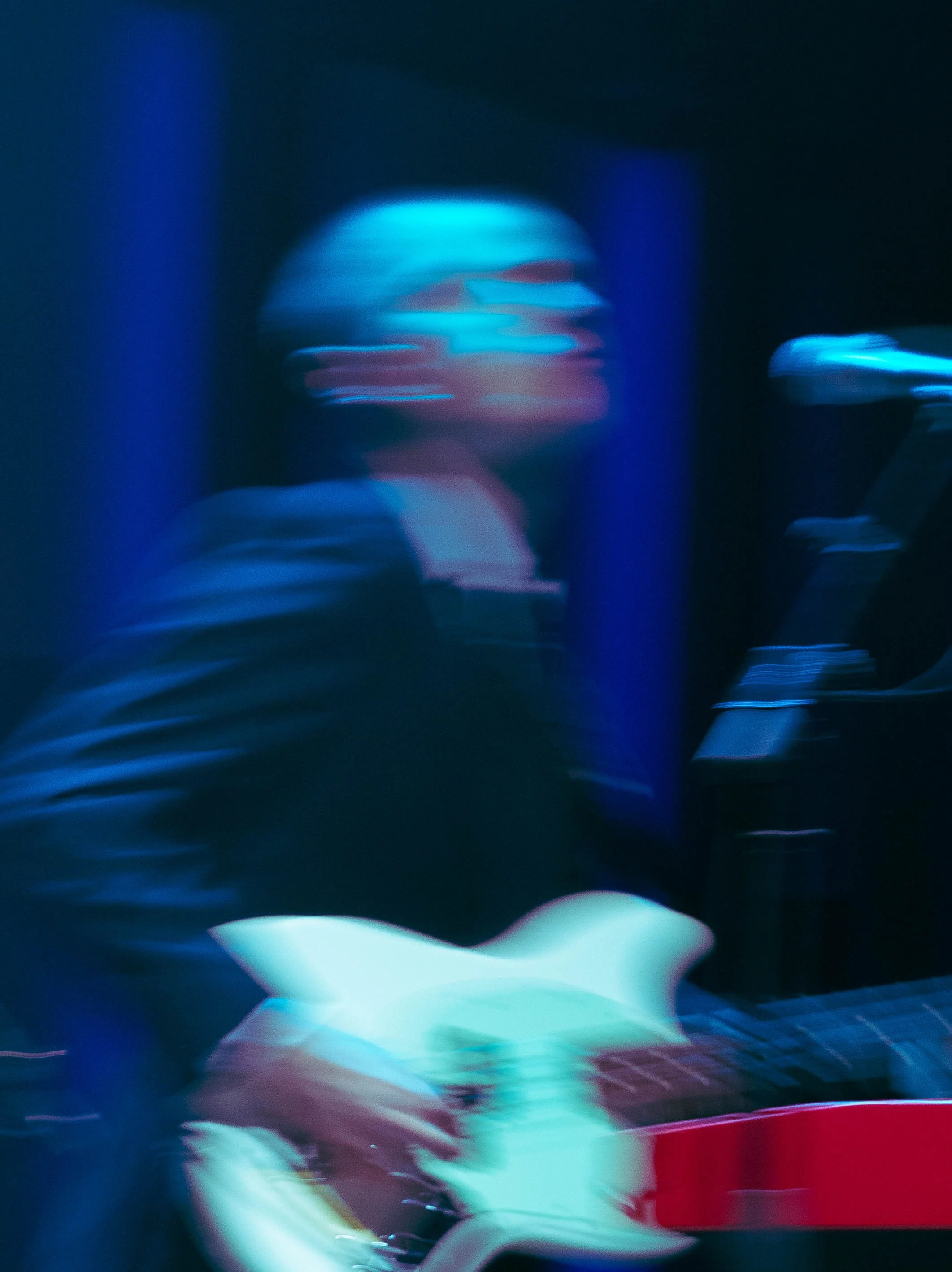 Blurry image of a musician playing electric bass with blue and dark lighting.