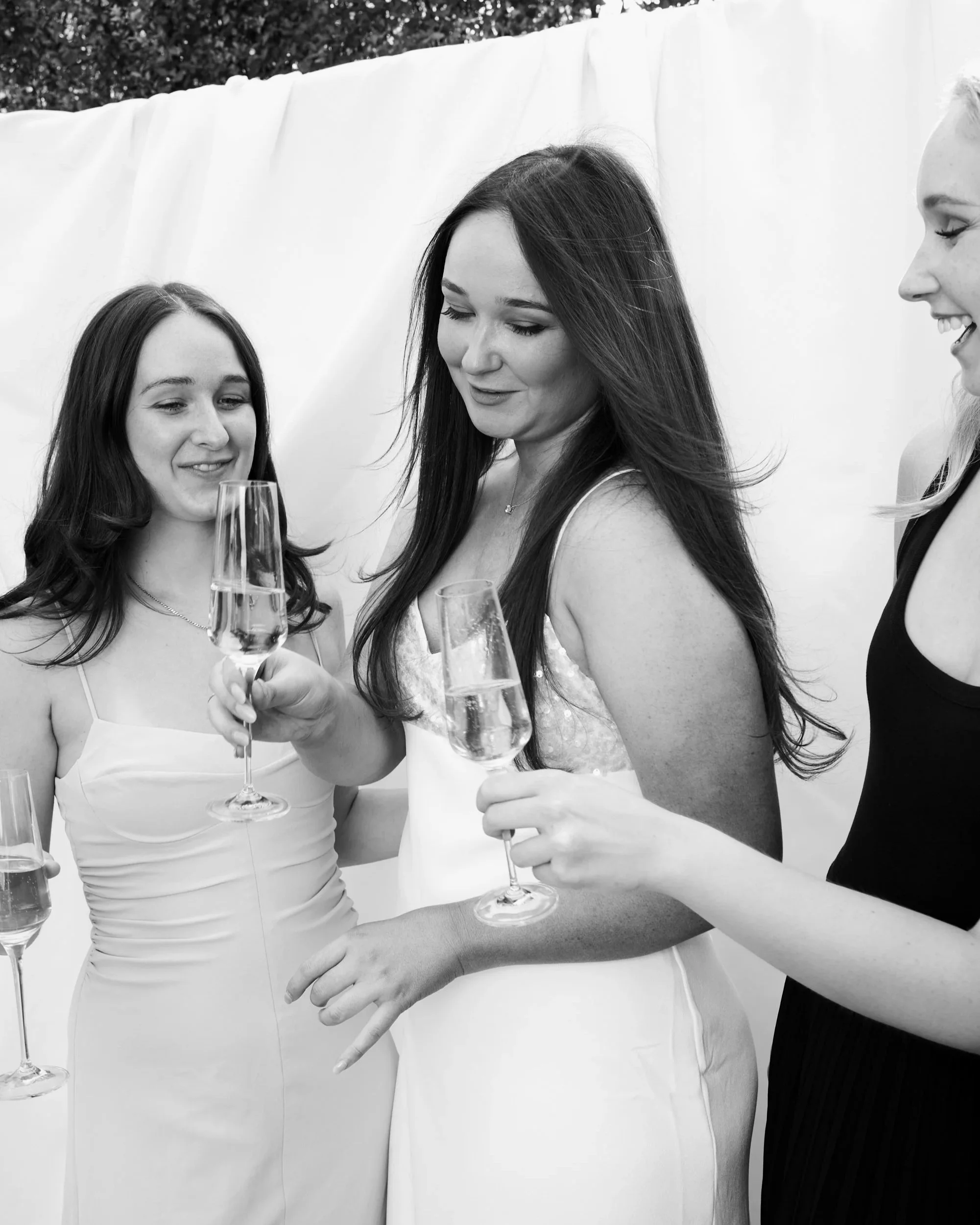 Three women in elegant dresses celebrating with champagne glasses outdoors.