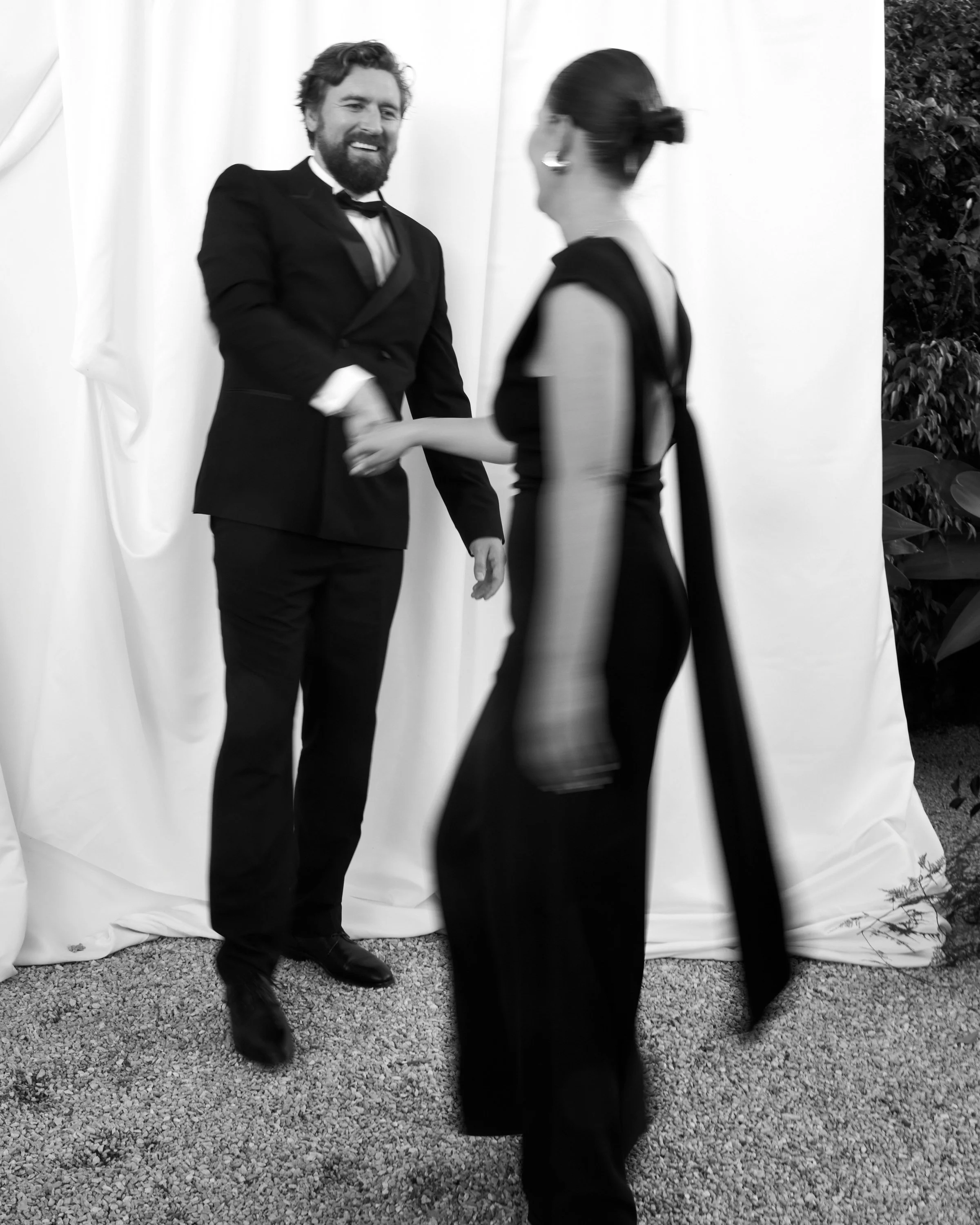 A man in a tuxedo shaking hands with a woman in a formal black dress at a formal event.