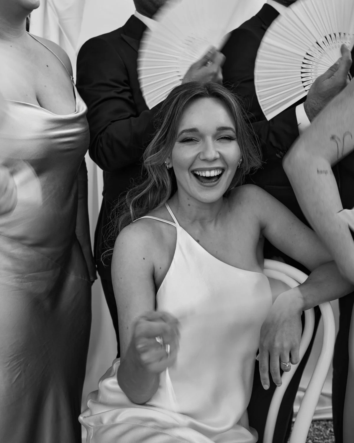 A woman with long hair and a dress, smiling and giving a thumbs-up, surrounded by people holding fans and dressed formally.