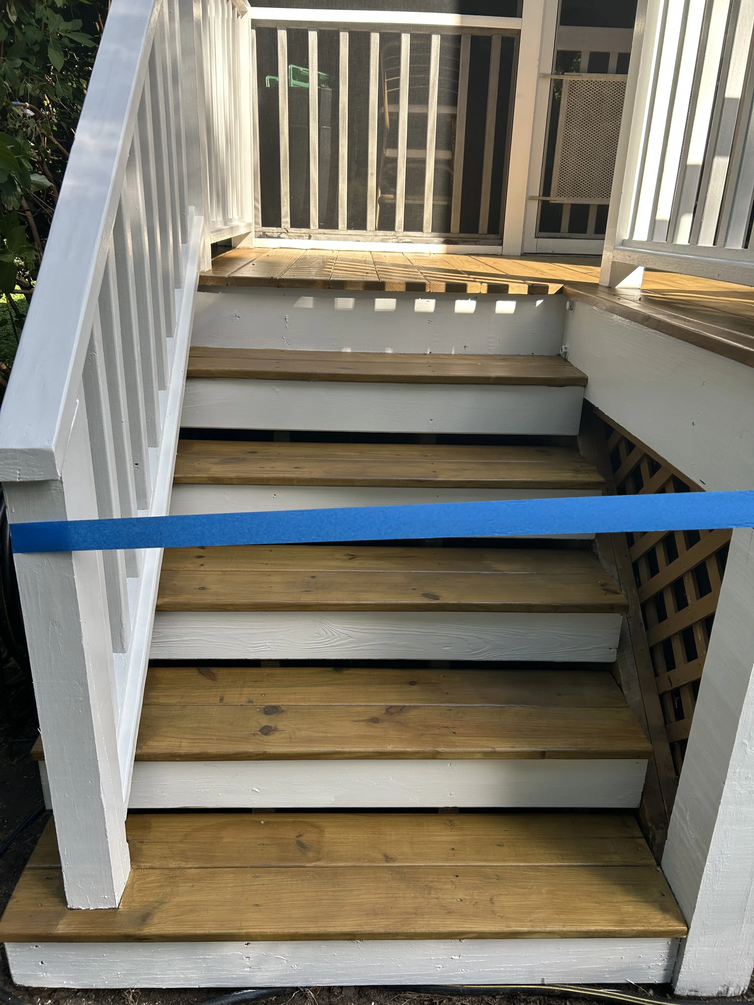 Wooden outdoor staircase with white railing and new wooden steps leading up to a small deck.