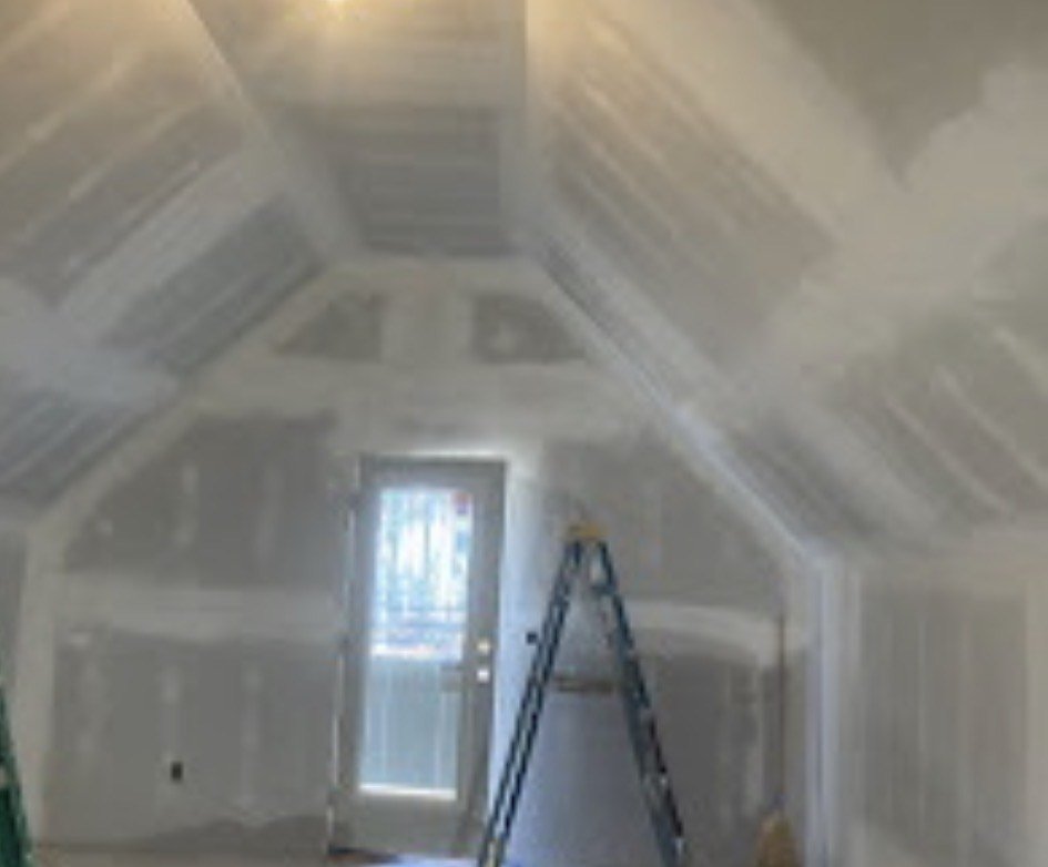 Interior of a room under construction with drywall partially installed, a ladder, and a door leading outside.