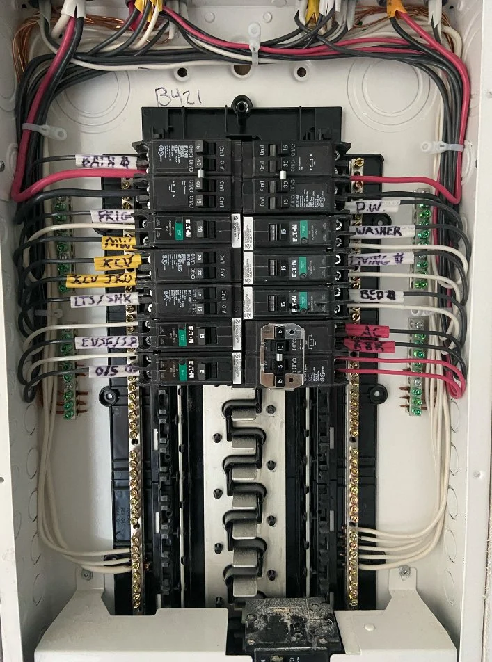 Electrical breaker box with multiple circuit breakers, wiring, and labels for different appliances and circuits.