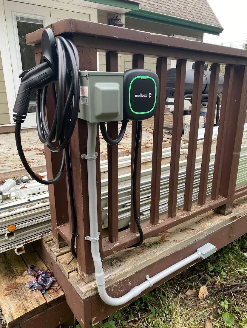 Electric vehicle charging station installed on a wooden deck outside a house, with charging cables hanging from the station.