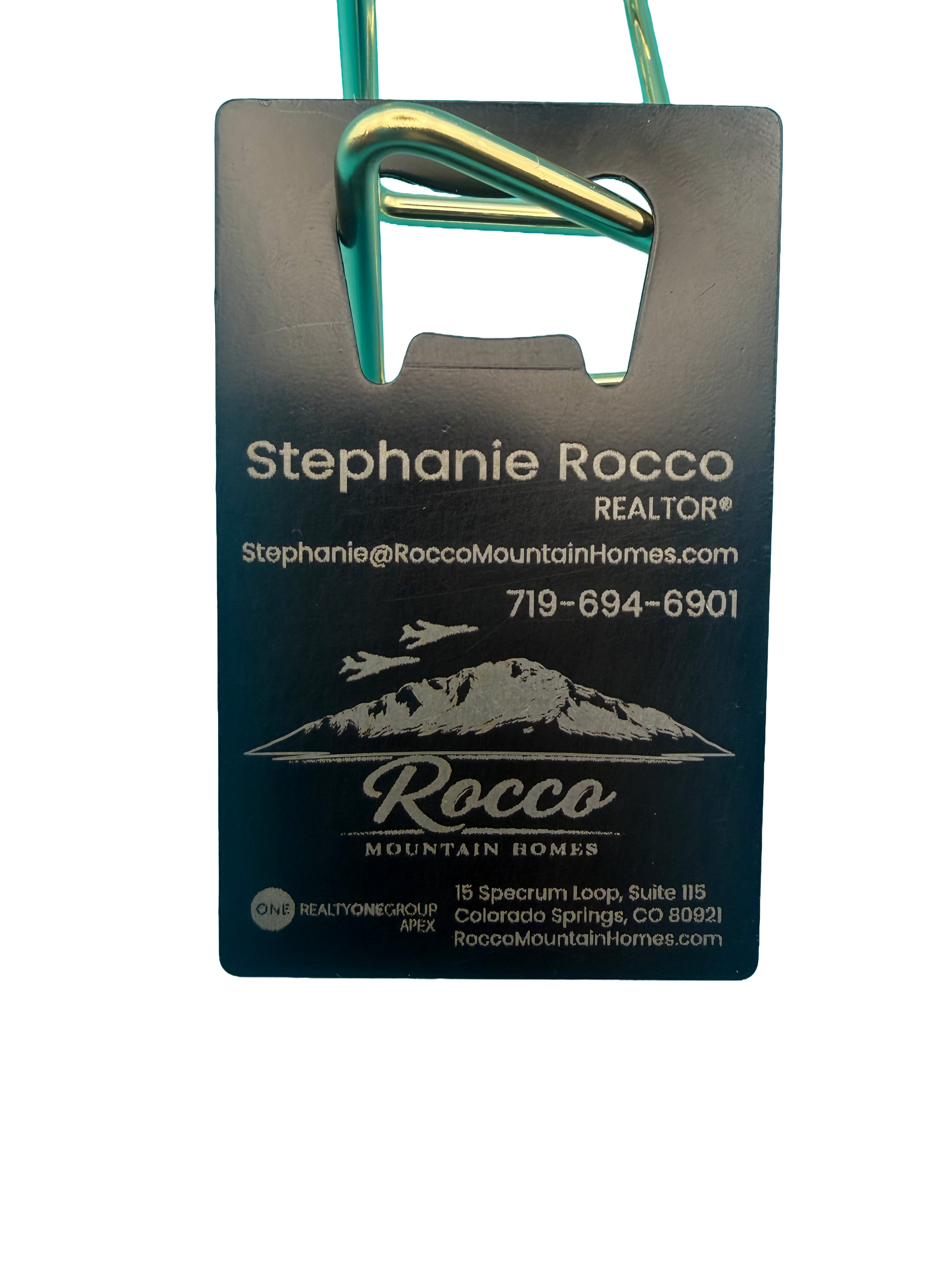 Close-up of a name tag with a mountain and airplane graphic, displaying contact information for Stephanie Rocco, a realtor specializing in mountain homes in Colorado.