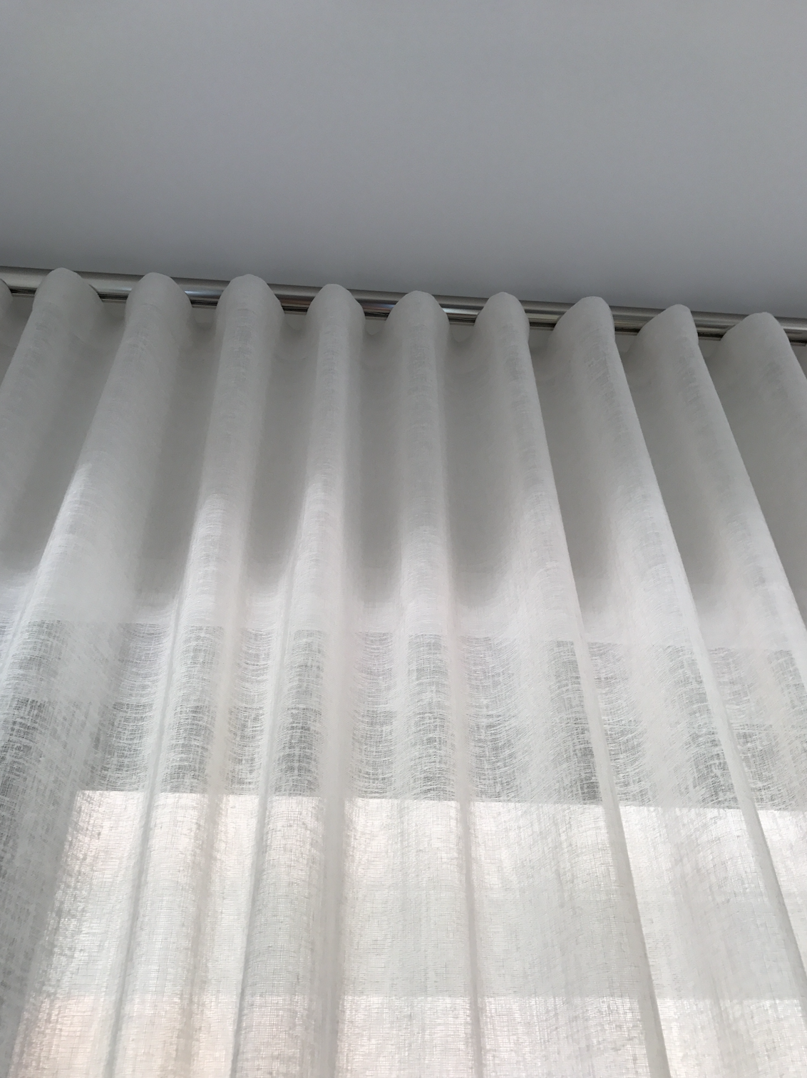 White sheer curtains hanging from a ceiling-mounted curtain rod.