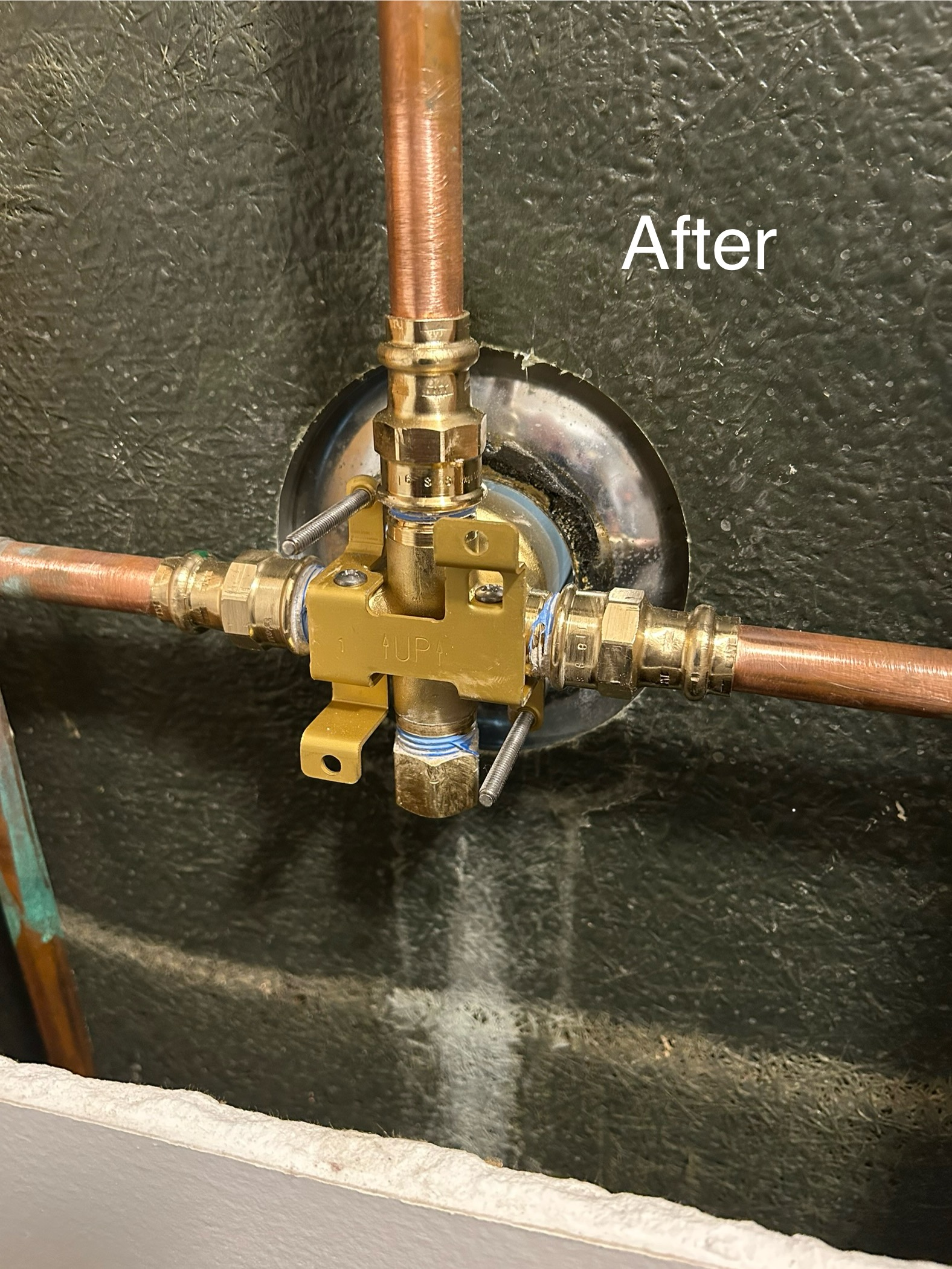 New plumbing valve connection with copper pipes and brass fittings installed in a wall.