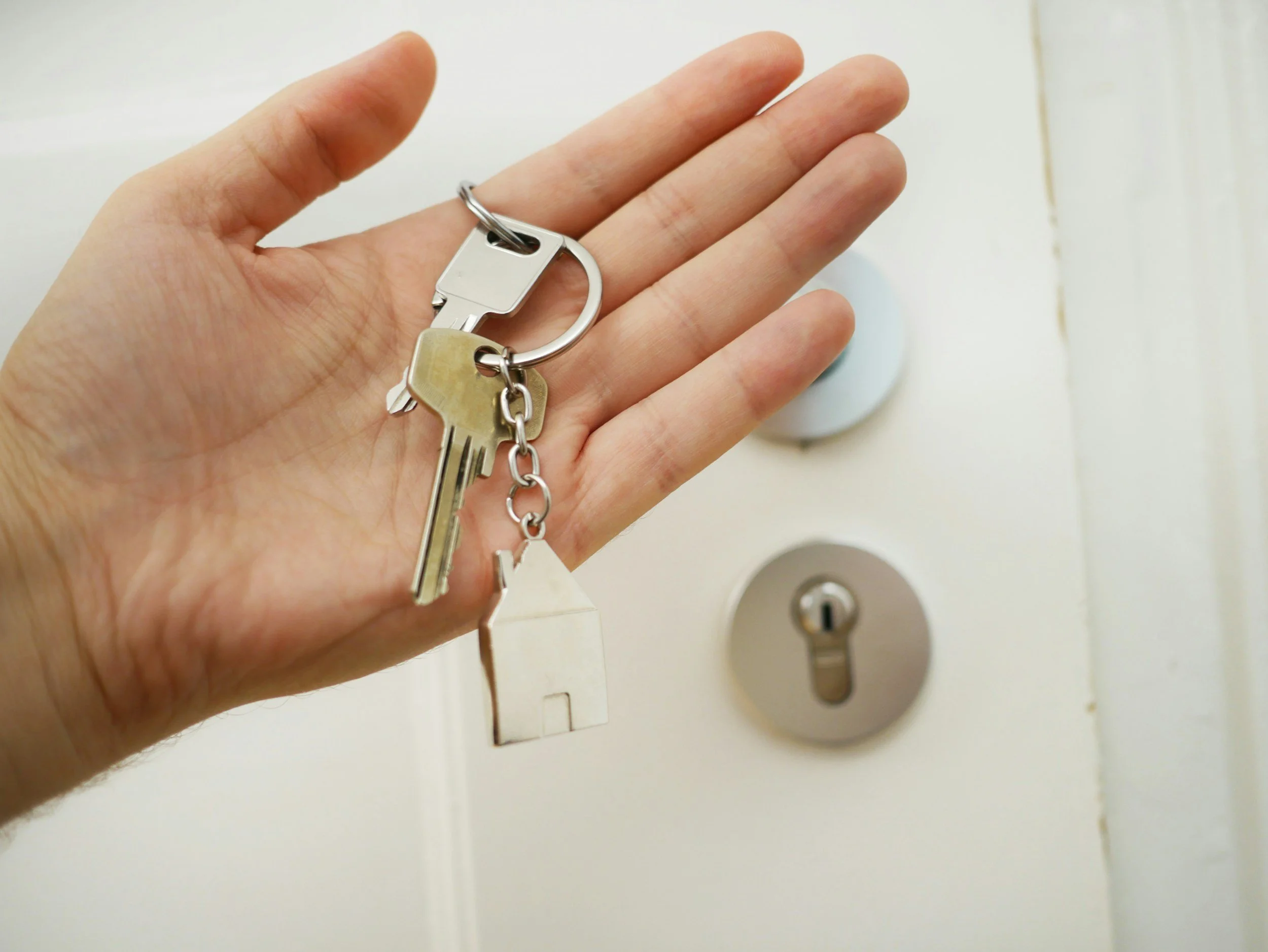 Hand holding a keychain with house-shaped and regular keys in front of a door lock.