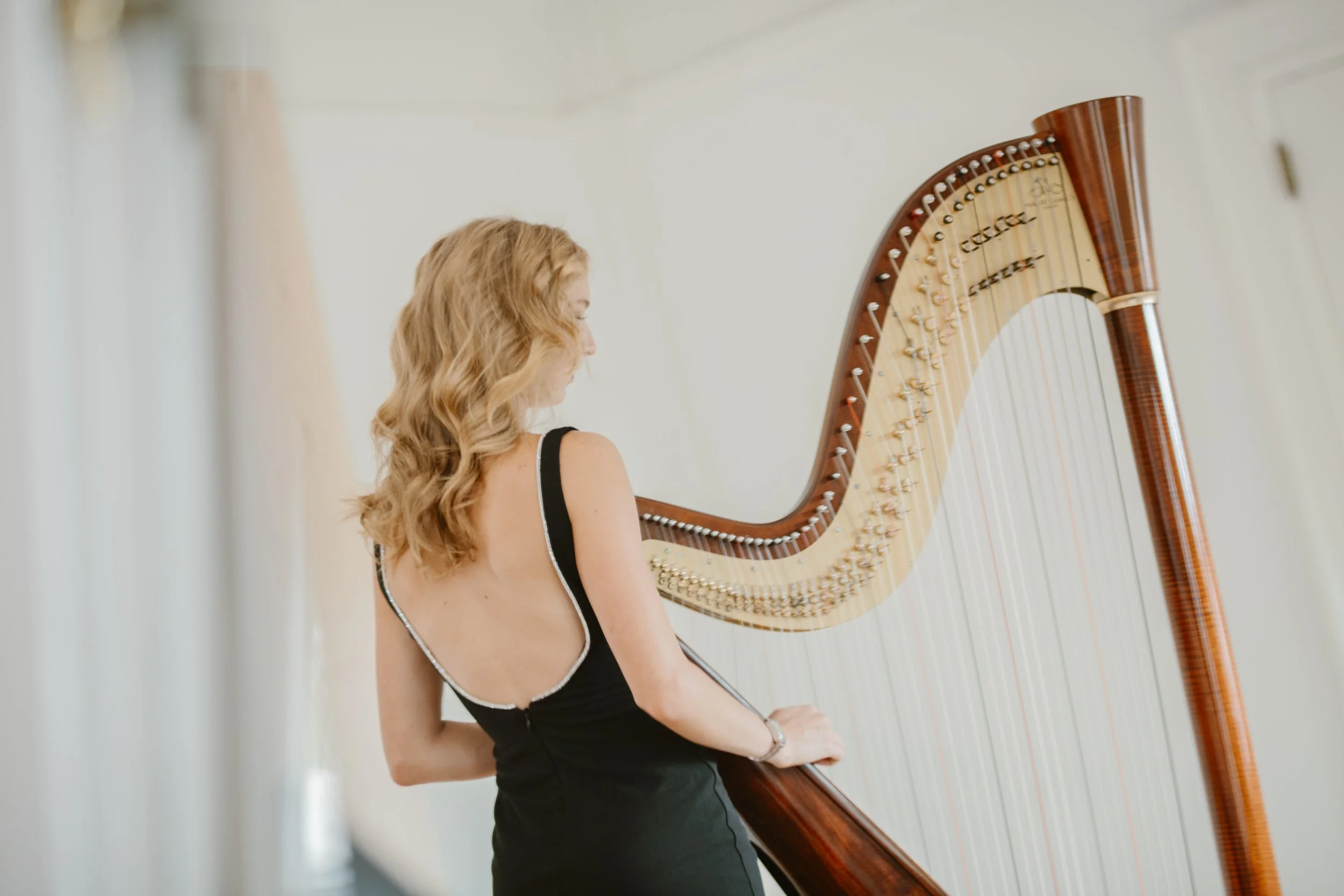 A woman with wavy blonde hair in a black dress playing a harp.