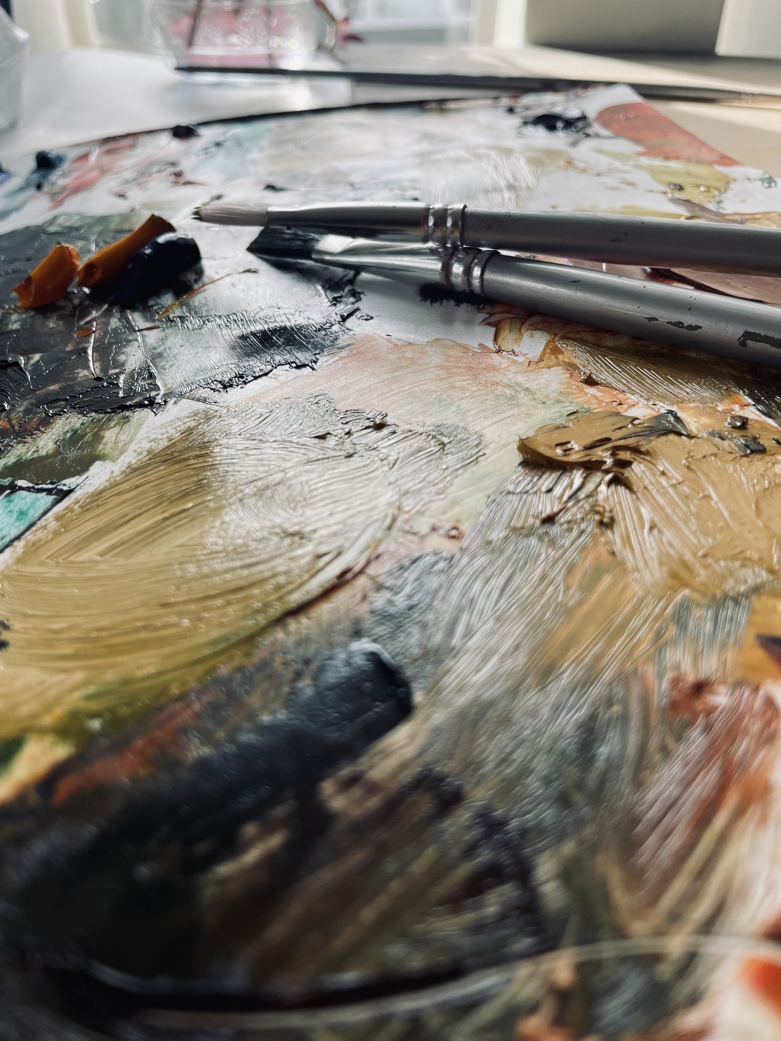 Close-up of an artist's palette with mixed oil paints in various colors, with two paintbrushes resting on top.