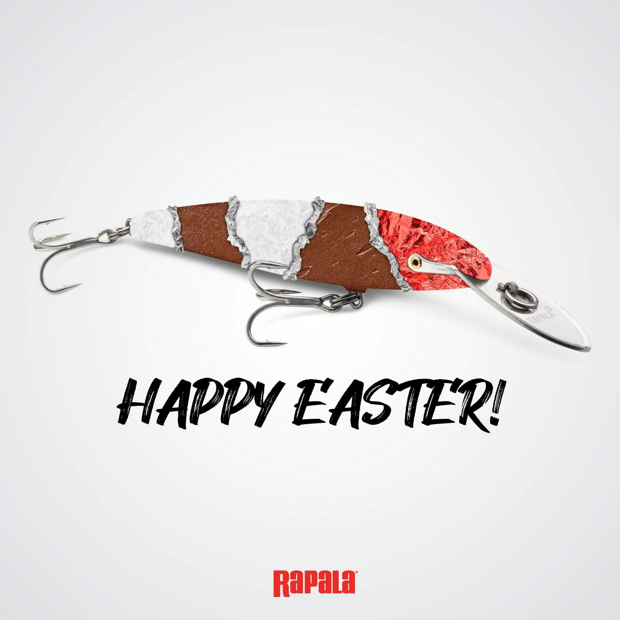 A fishing lure designed to look like a chocolate fish with a red head, white body, and brown tail, with multiple hooks attached. Text overlay says 'HAPPY EASTER!' and the Rapala logo at the bottom.