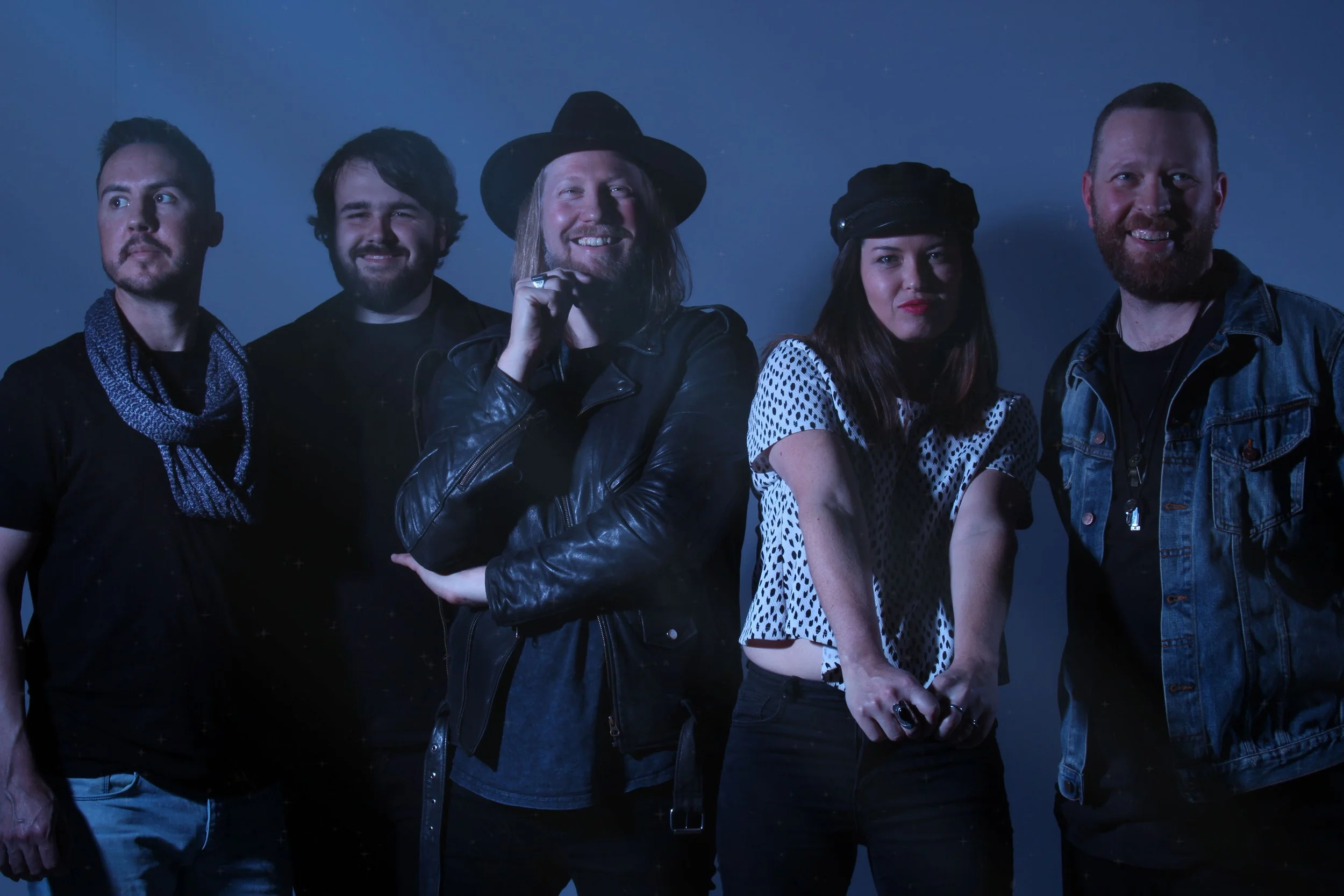 Group of five musicians posing against a dark background, dressed in casual and rock-inspired clothing.