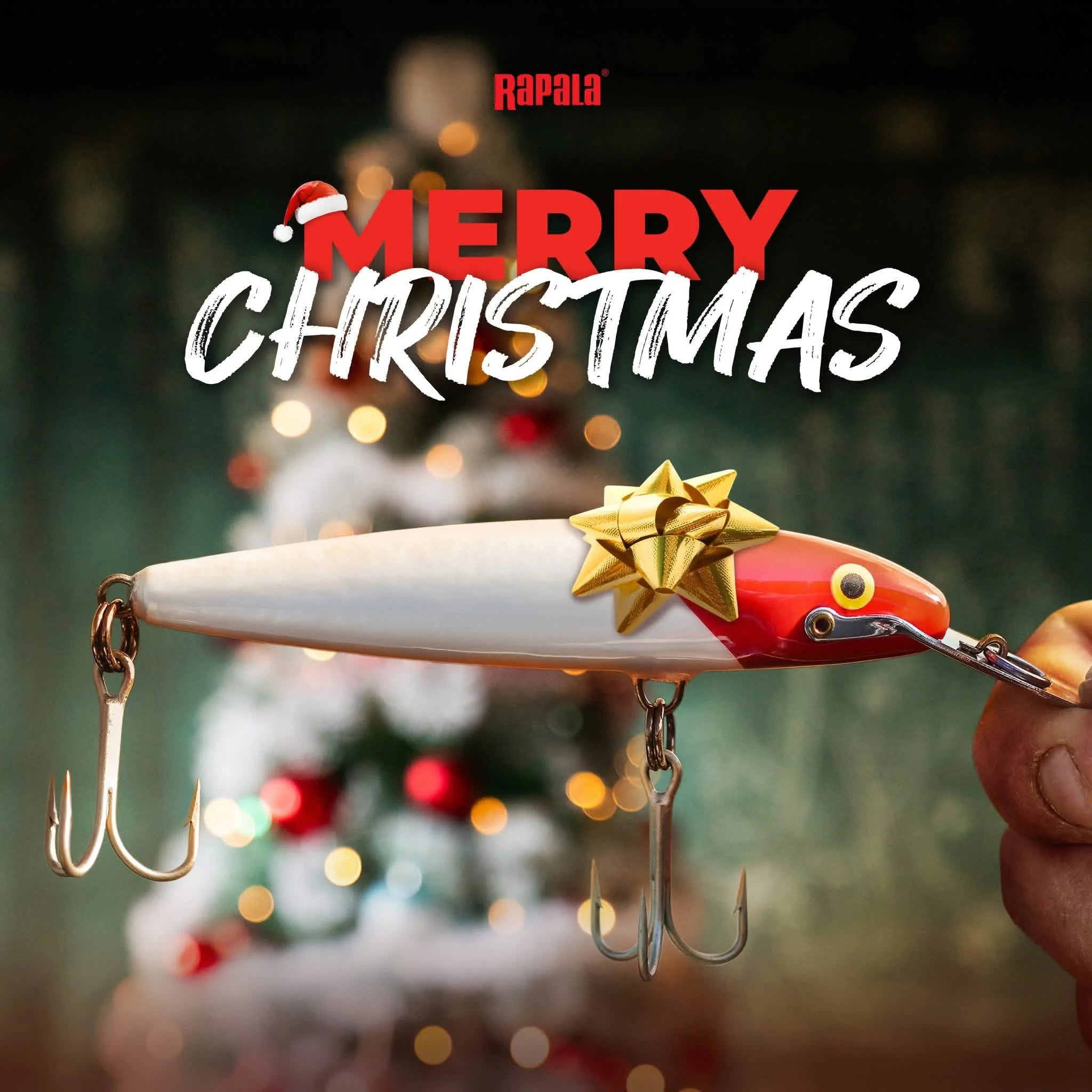 A fishing lure with a gold bow on top held by a person's hand, with a Christmas tree in the background, and the words 'Merry Christmas' and 'Rapala' on the image.