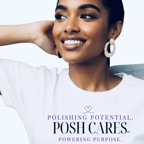 A smiling woman with dark hair, wearing large hoop earrings and a white shirt, posing with her hand behind her head against a plain light background.