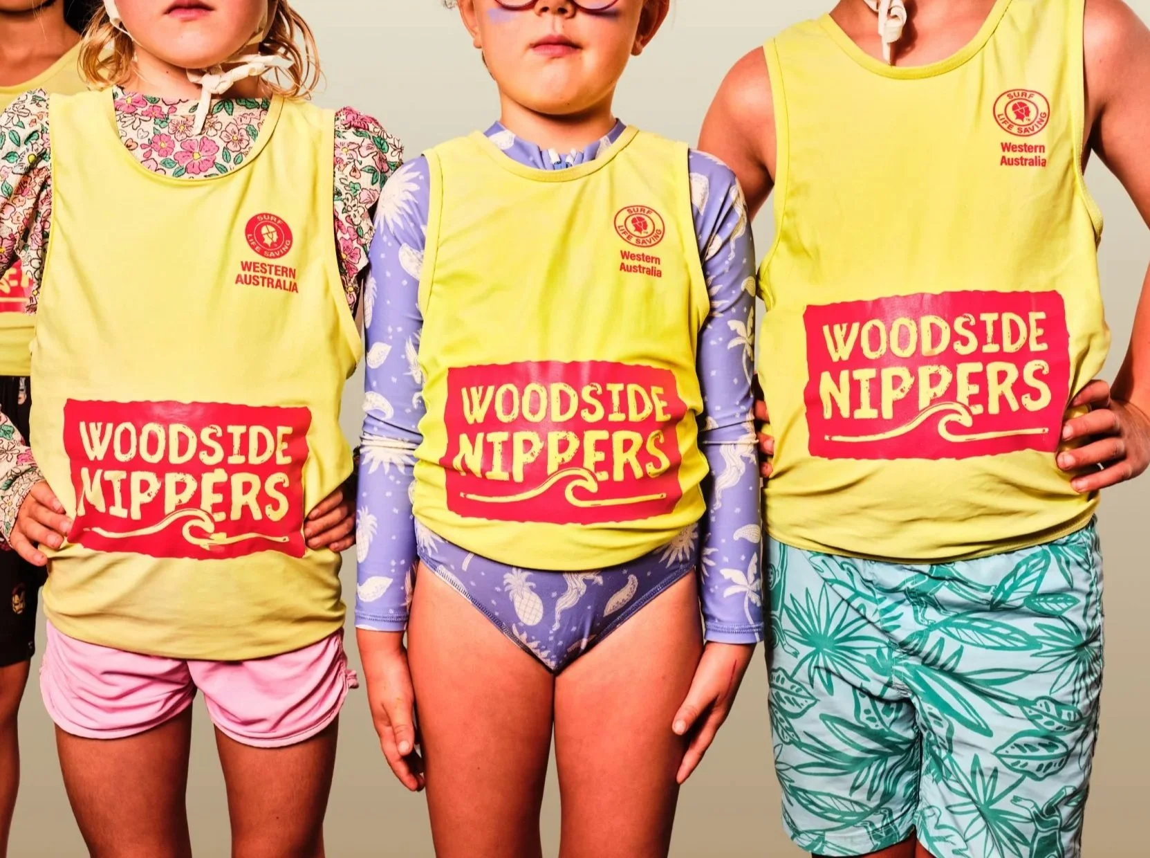 Children in Surf Life Saving WA vests and caps displaying fossil fuel polluter Woodside's logo