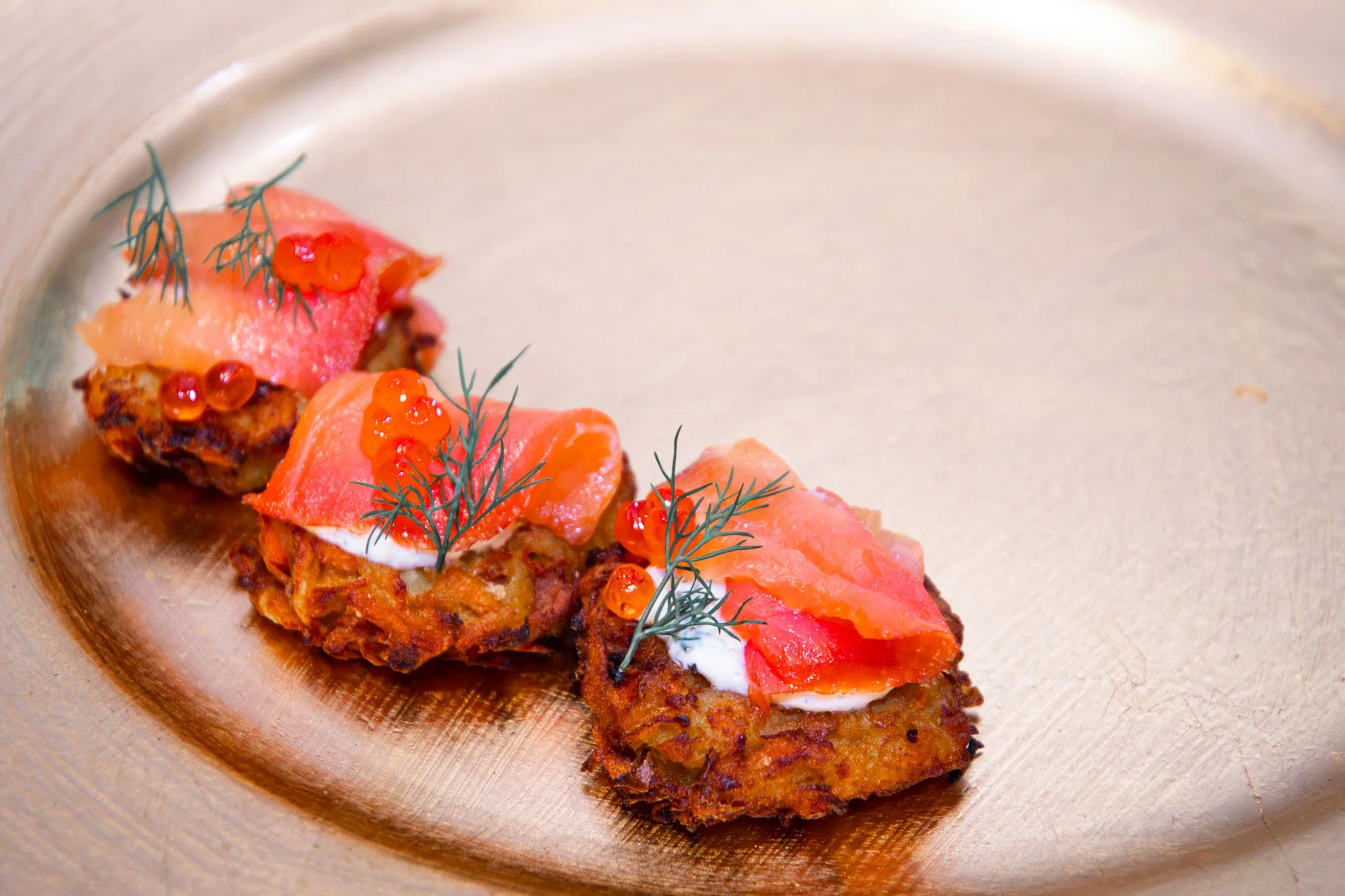 Three pieces of croquettes topped with smoked salmon, fresh dill, and red caviar on a beige ceramic plate.