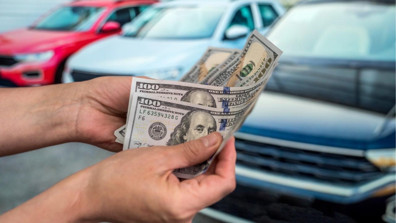 A person holding $100 bills in front of vehicles, illustrating how Cash For Junk Cars NW pays cash on the spot.